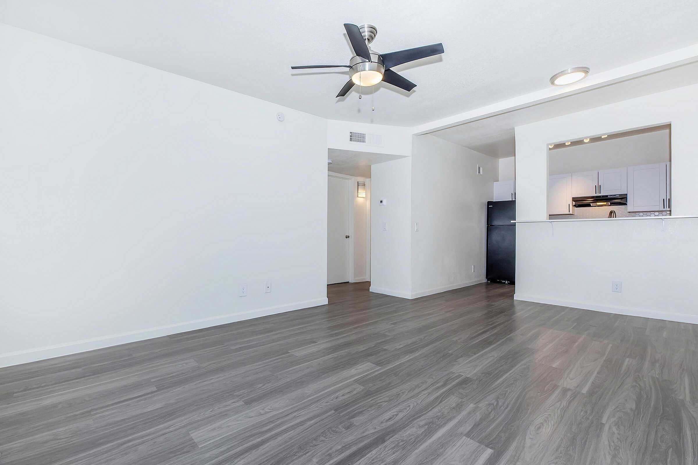 Modern open-plan apartment with sleek hardwood floors, ceiling fan, and stylish kitchen entry.
