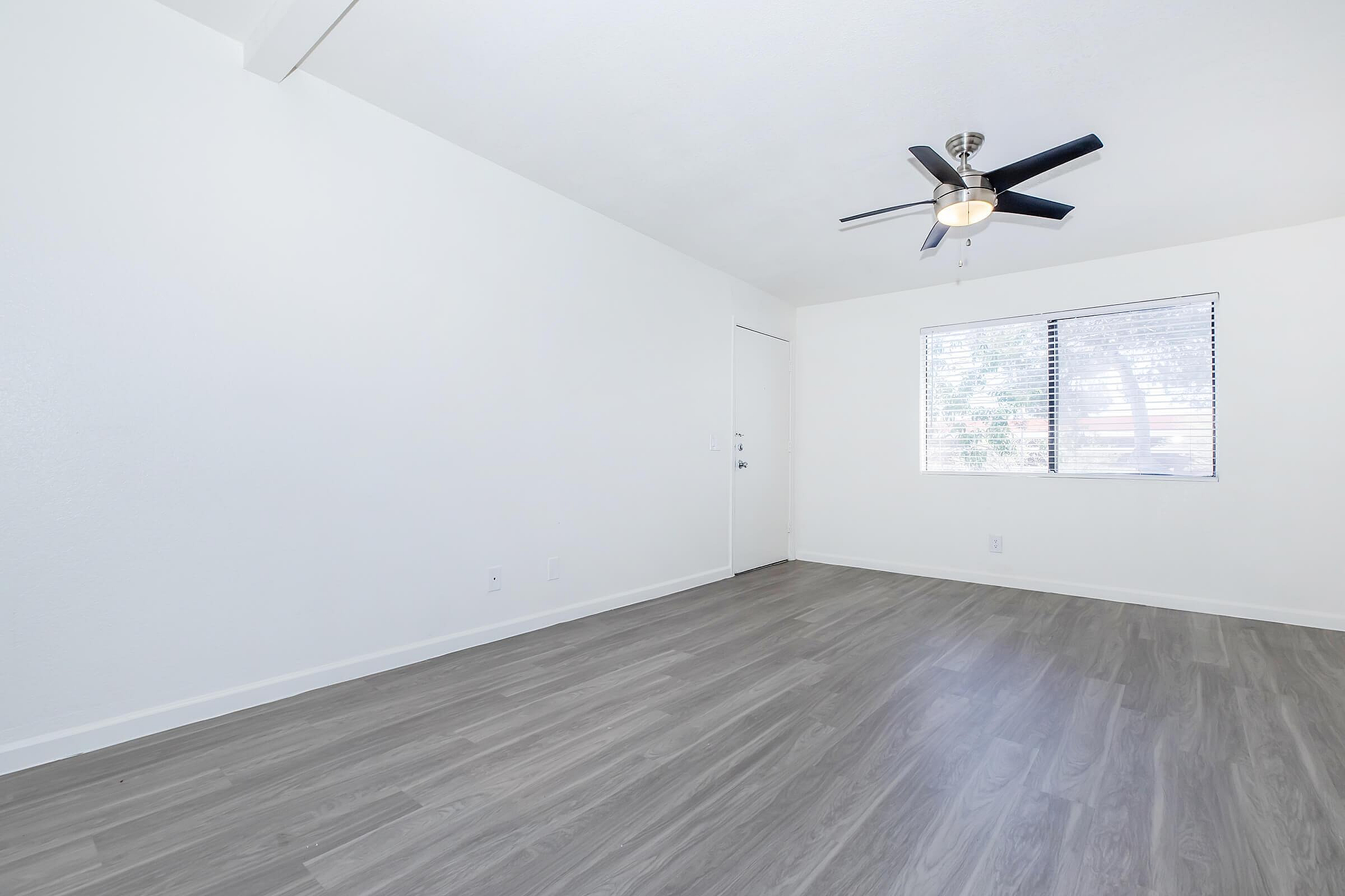 Spacious room with sleek wooden floors, modern ceiling fan, and large window offering abundant natural light.