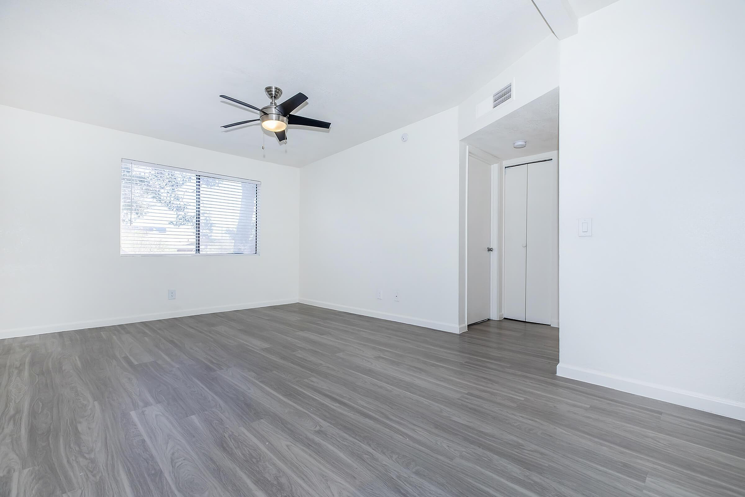 Bright, spacious room with modern ceiling fan and sleek wood flooring, featuring a large window allowing natural light.