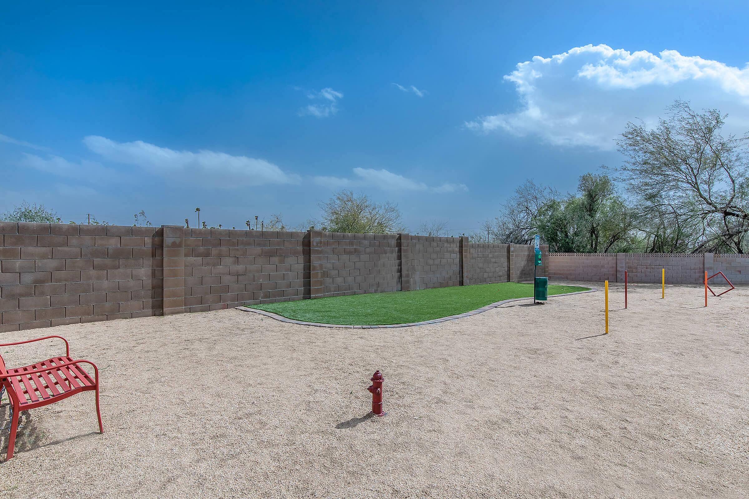 Inviting outdoor dog park with vibrant green grass, agility poles, and a bright red bench under a clear blue sky.