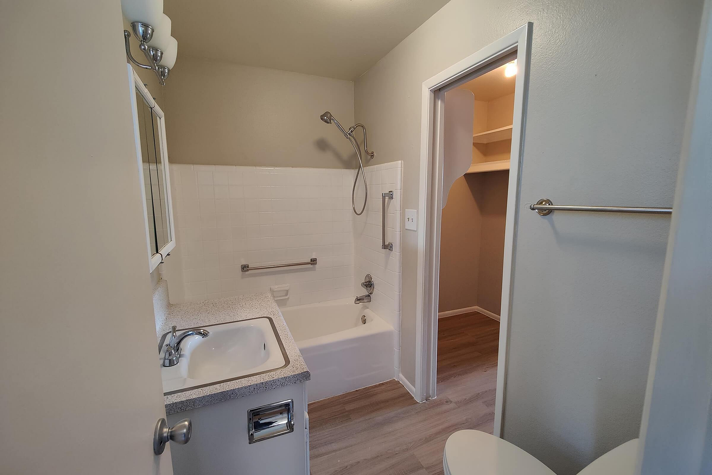Inviting bathroom with a modern tub, sleek countertop, large mirror, and elegant lighting, leading to a spacious walk-in closet.