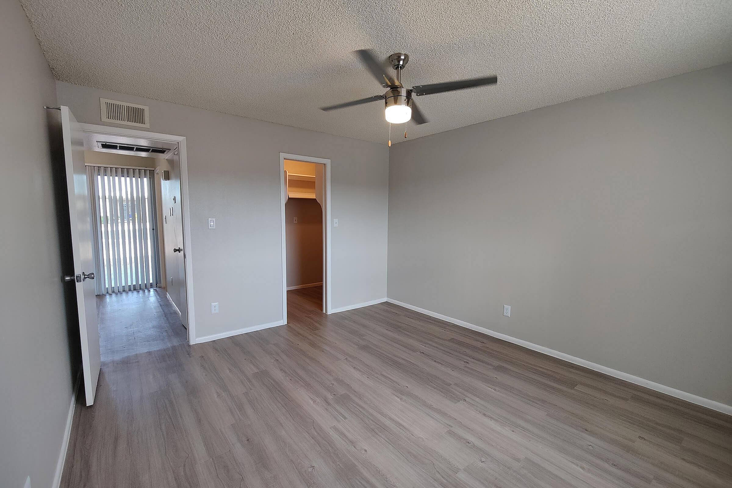 Spacious bedroom with elegant wood flooring, ceiling fan, and abundant natural light through sliding glass doors.