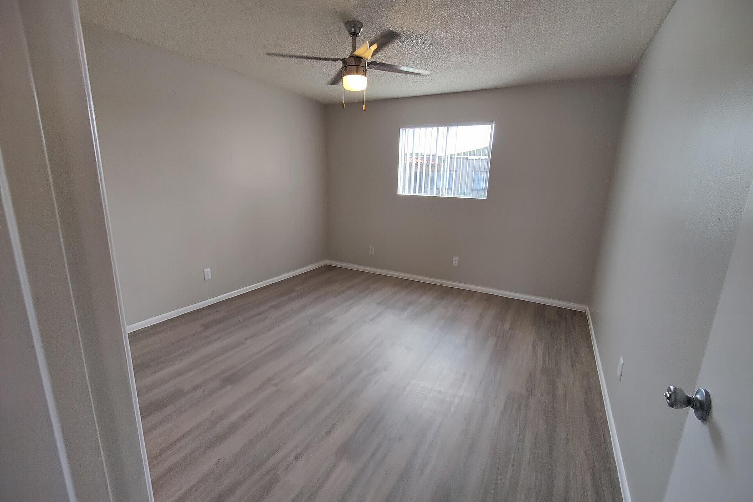 Bright, spacious bedroom with elegant wood flooring and a modern ceiling fan, enhanced by natural light from a large window.