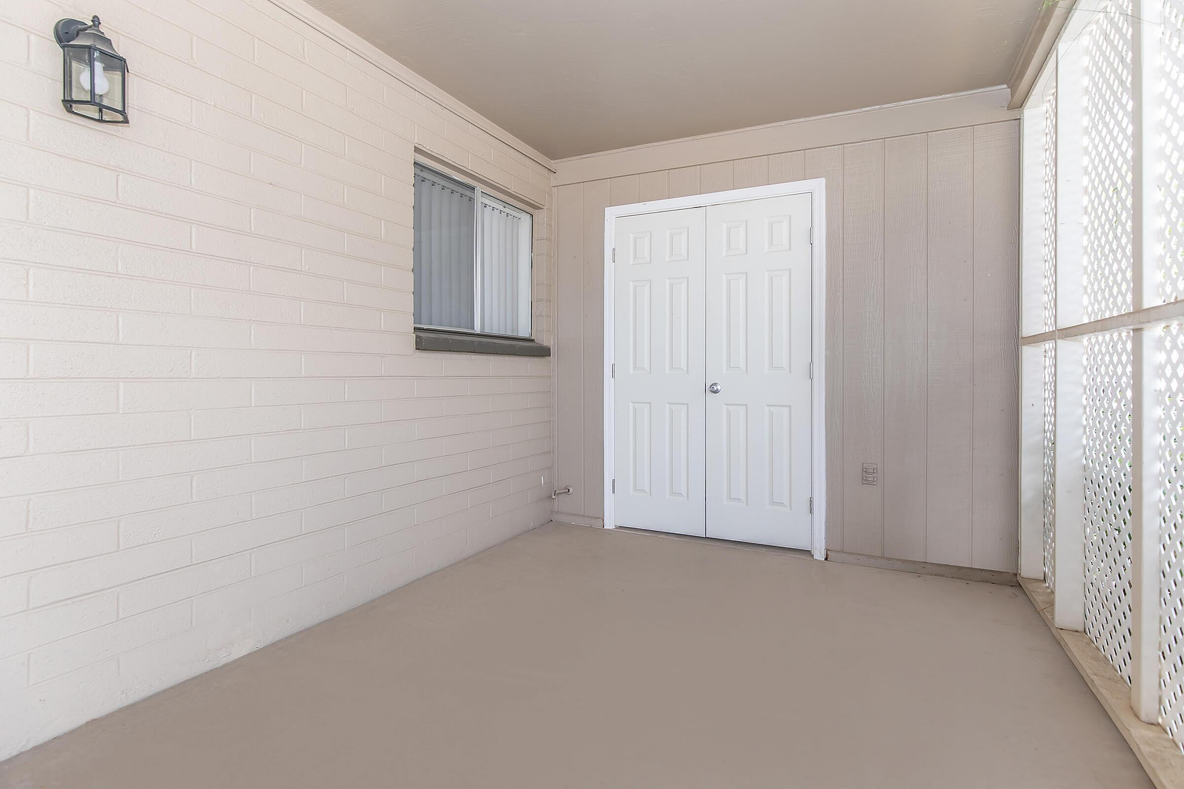 Bright and inviting enclosed patio featuring textured white brick walls, a stylish light fixture, and double doors providing access to indoor comfort.