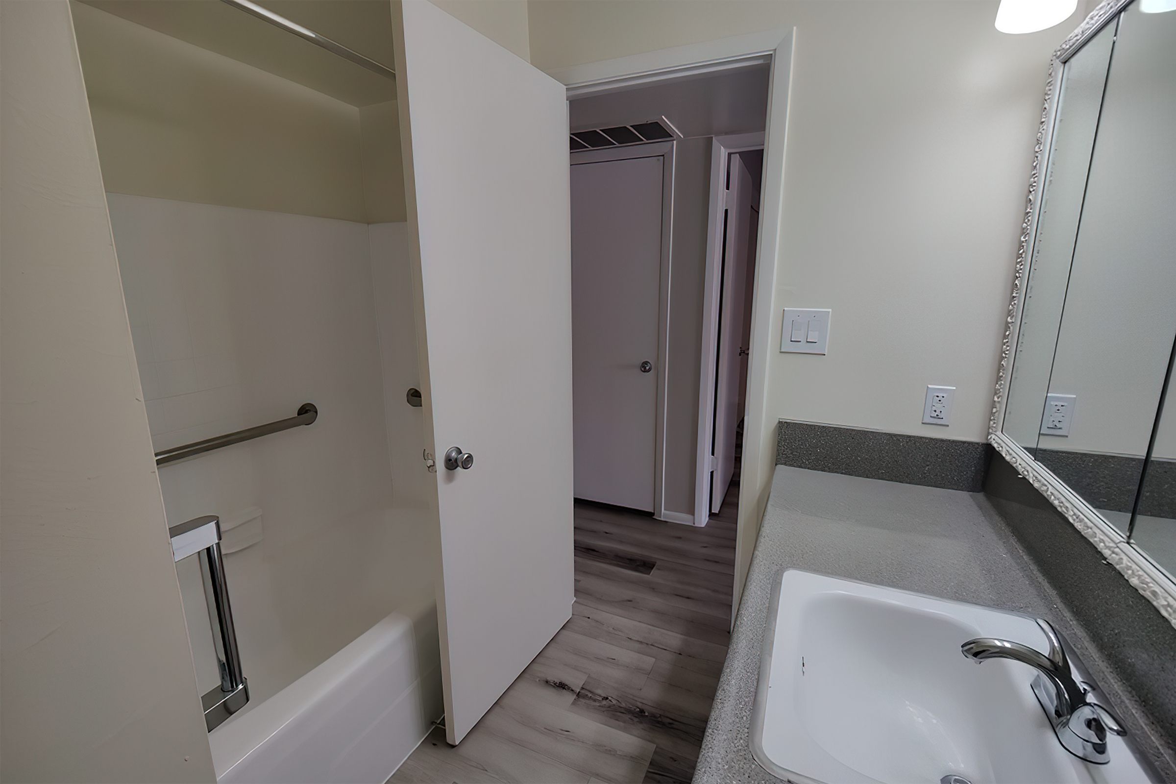 Sleek bathroom with modern fixtures, featuring a spacious vanity, illuminated mirror, and a cozy bathtub with grab bars.