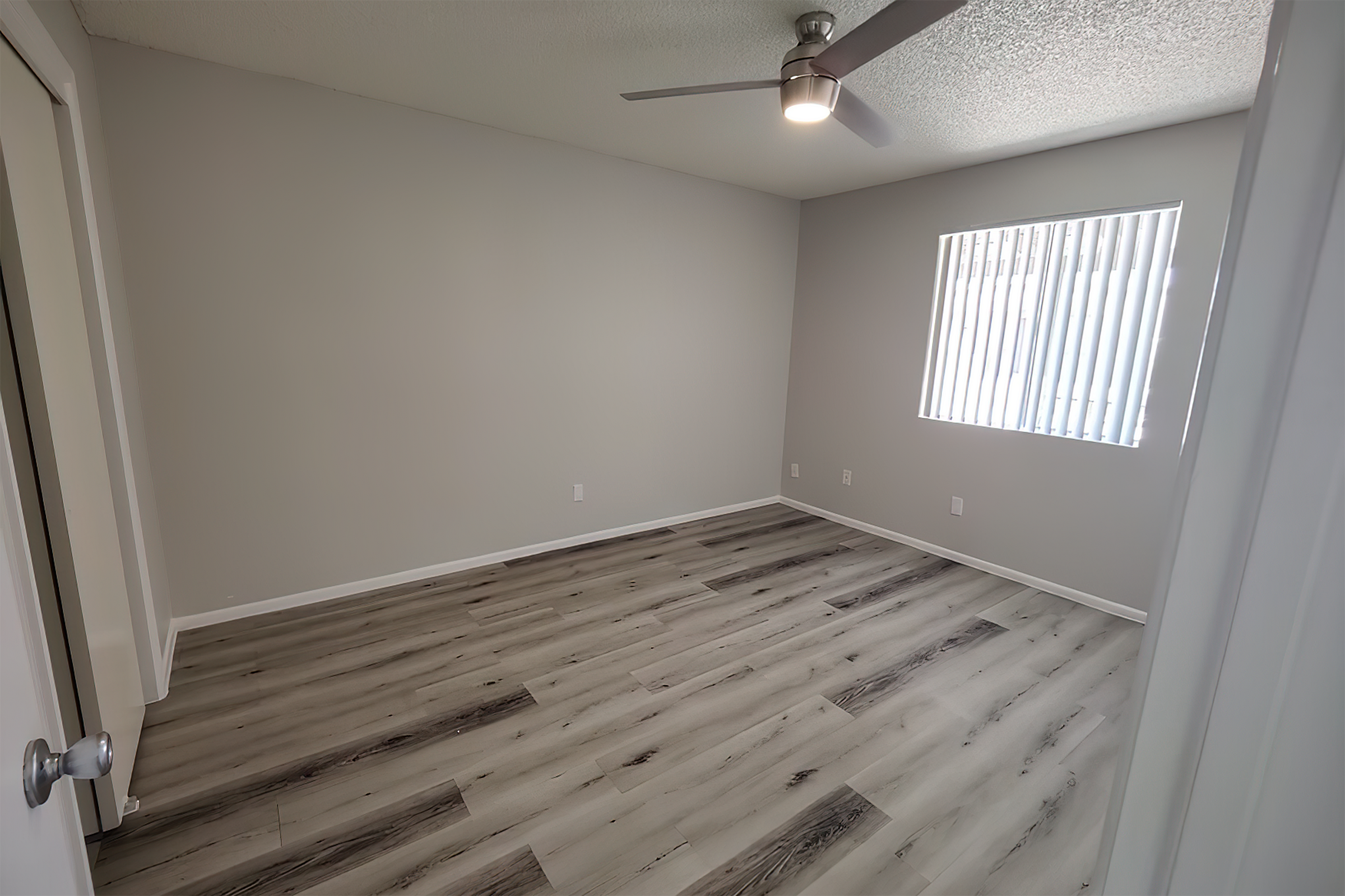 Bright and modern bedroom with elegant light wood flooring, a sleek ceiling fan, and ample natural light from a large window.