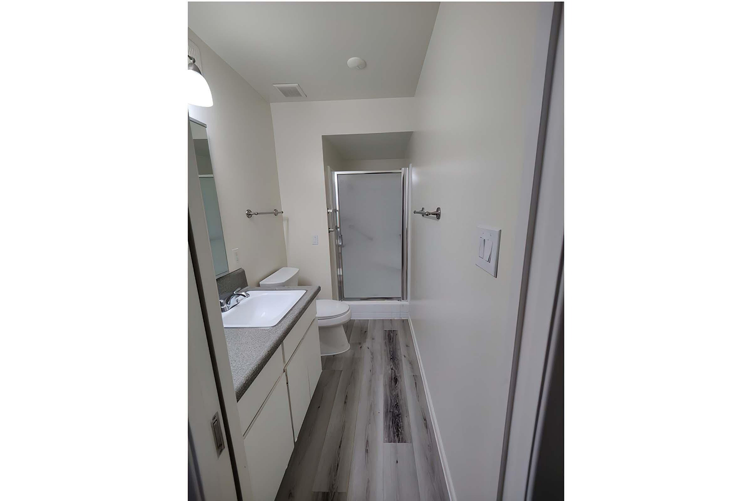 Modern bathroom featuring sleek surfaces, a spacious vanity, and a glass-enclosed shower, illuminated by stylish lighting.