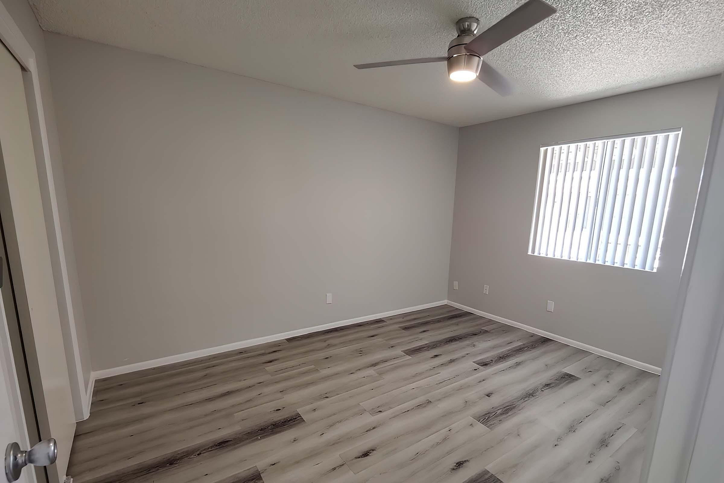 Bright and spacious bedroom with modern flooring and a sleek ceiling fan, inviting natural light through the large window.