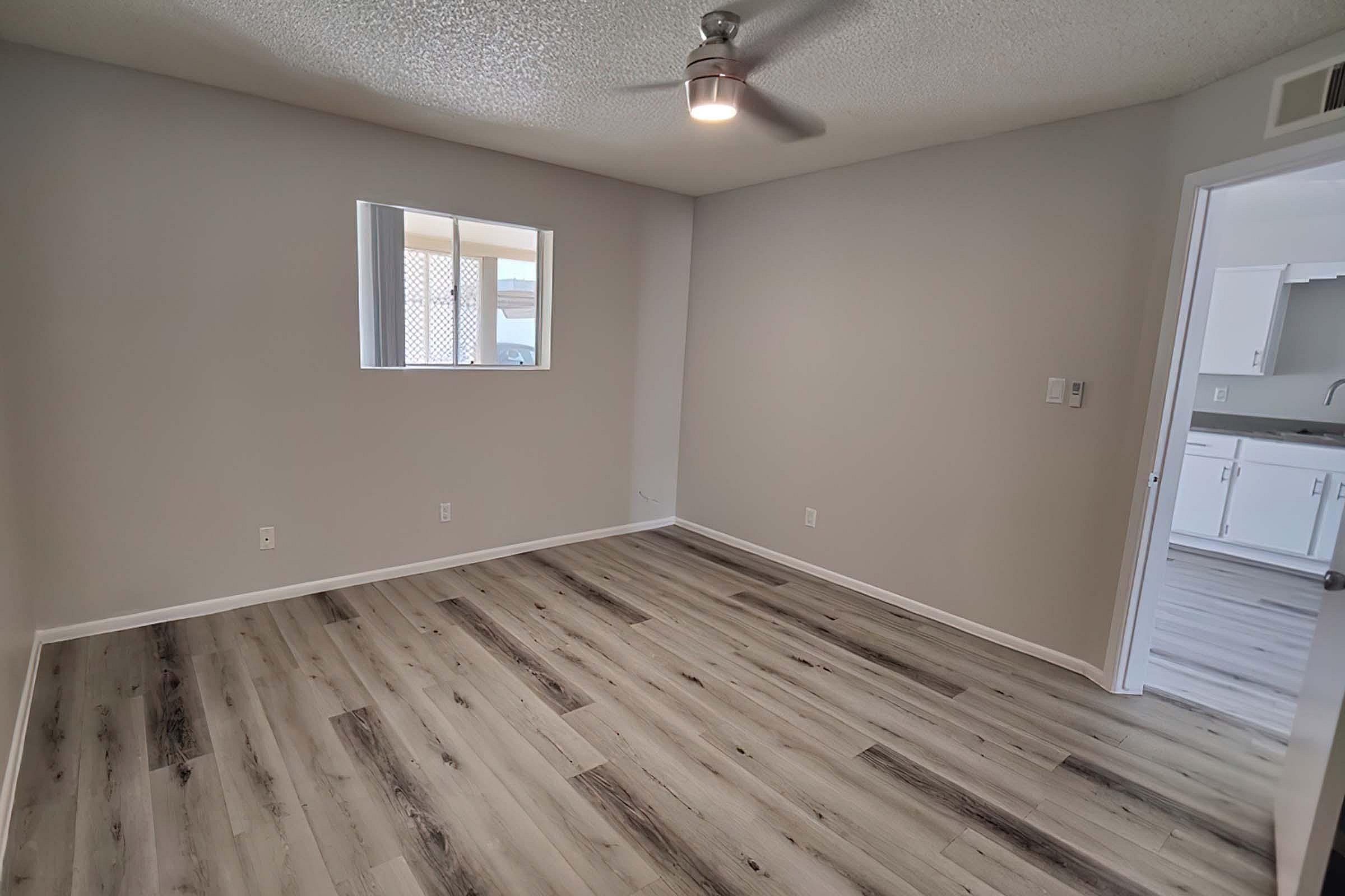 Modern and spacious bedroom with sleek laminate flooring and a ceiling fan, showcasing a bright and inviting atmosphere.