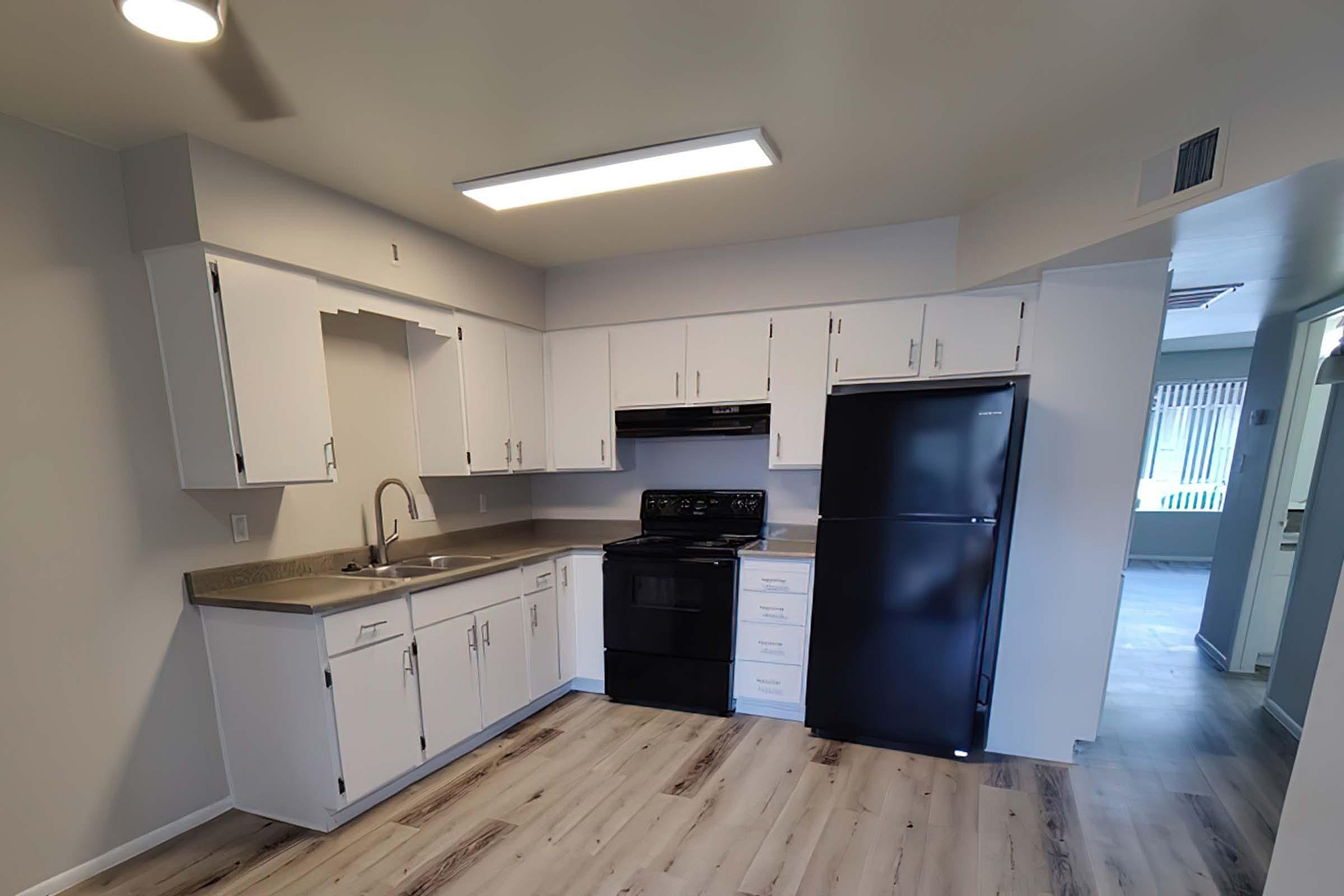 Modern kitchen with sleek white cabinetry, stylish dark appliances, and elegant wood flooring.