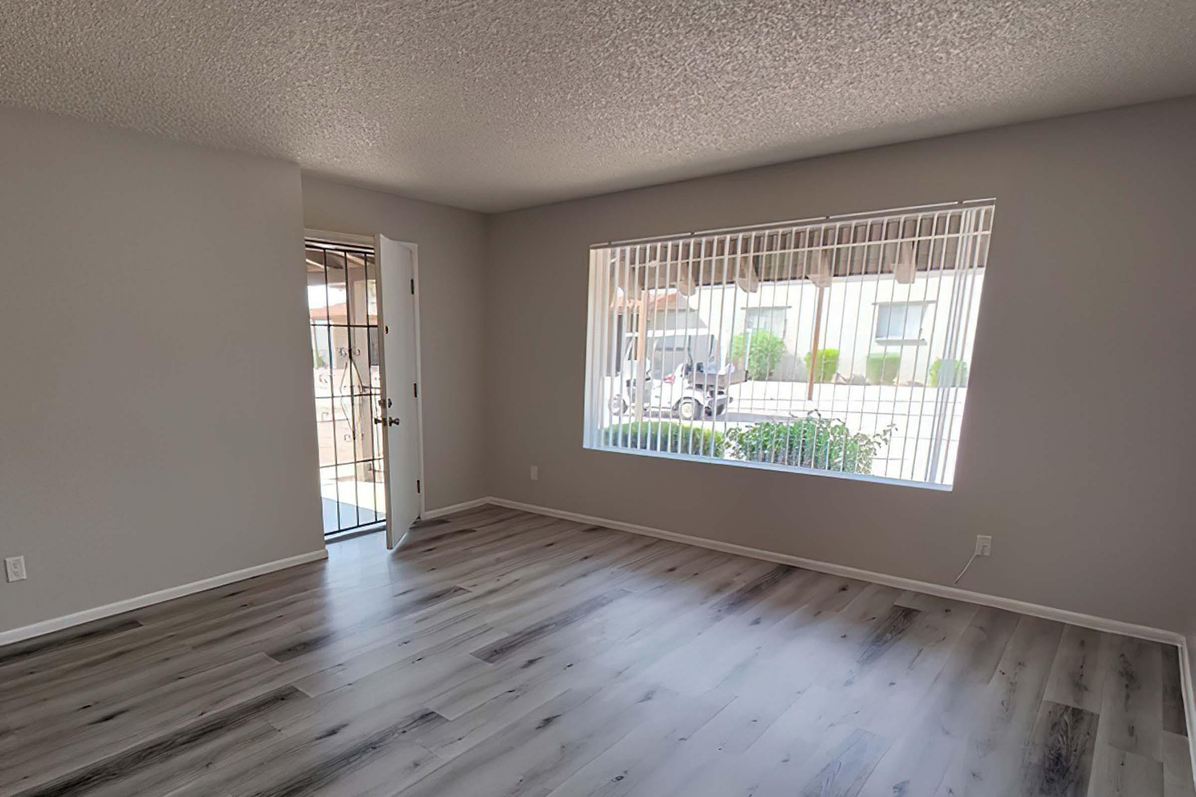 Bright and airy living room with modern wood floors, large windows, and inviting entryway, perfect for welcoming guests.
