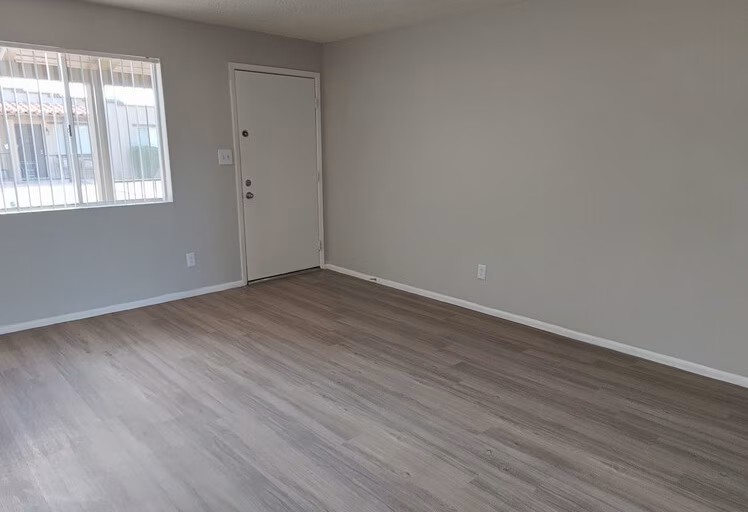 Bright and airy living room with sleek wood flooring and a large window, offering a welcoming and modern space.