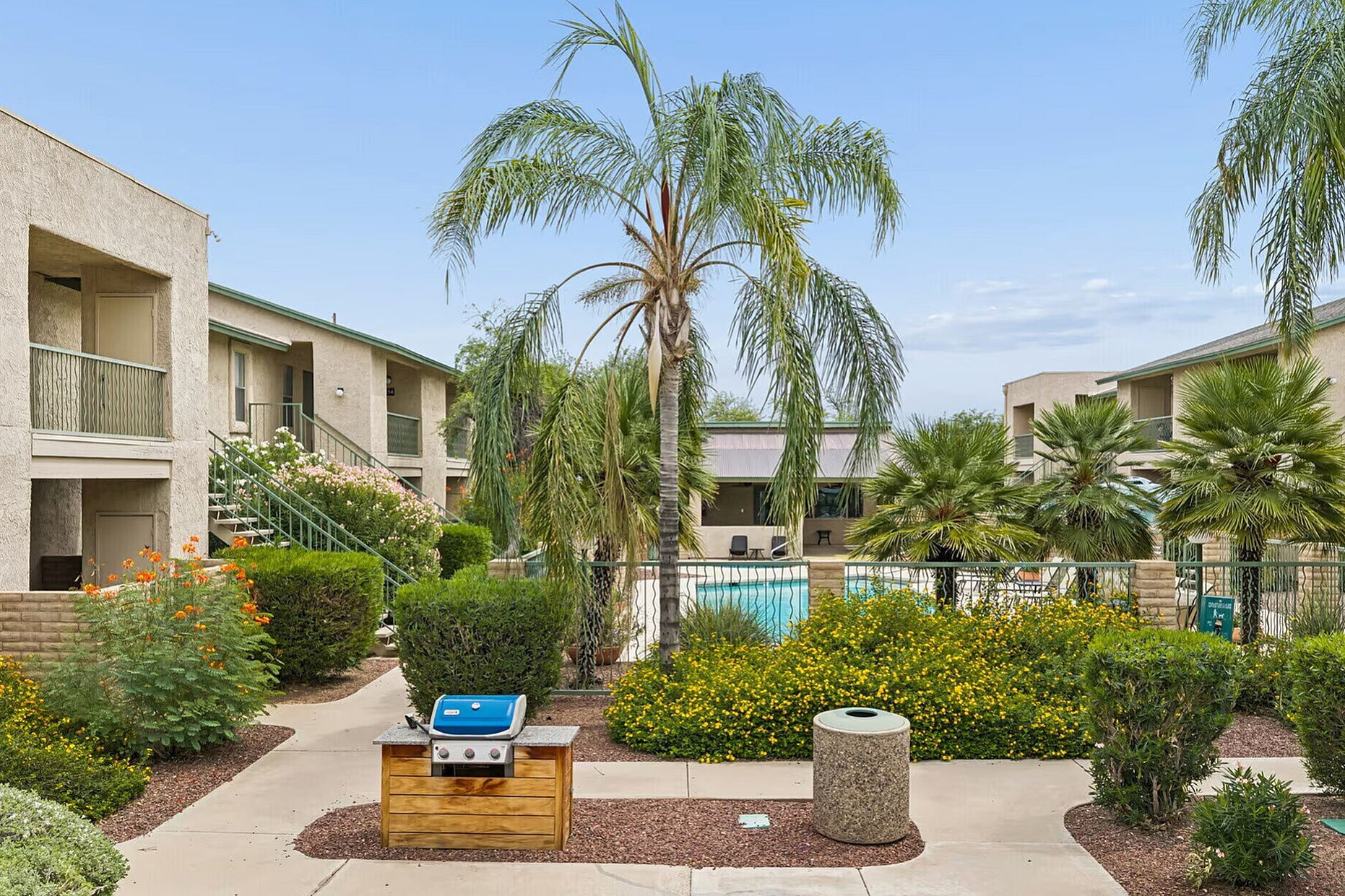 Charming apartment complex with lush landscaping, a sparkling pool, and a stylish BBQ area, perfect for outdoor gatherings and relaxation.