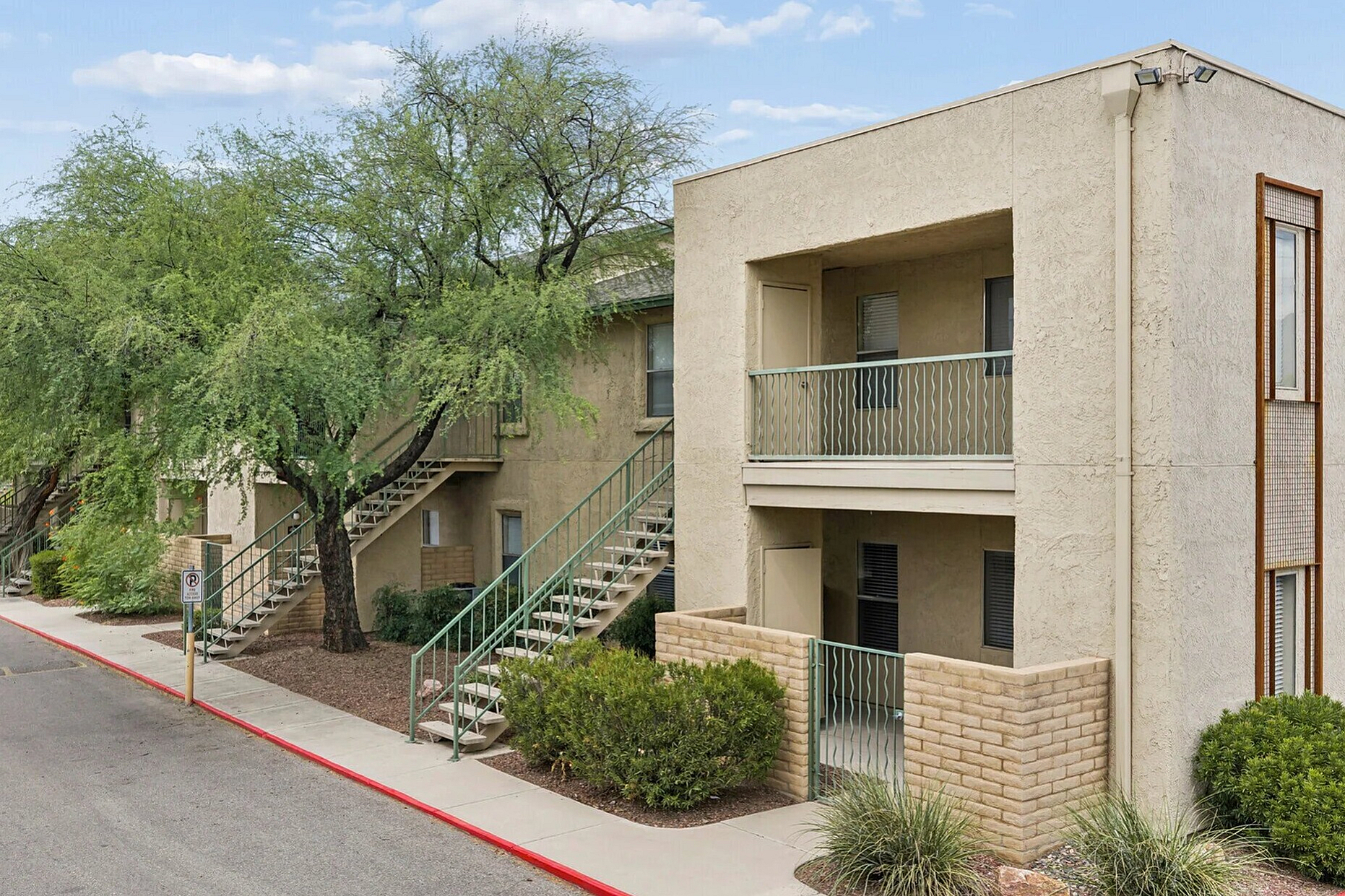 Charming apartment complex with lush greenery, outdoor stairs, and spacious balconies, offering a peaceful and inviting environment.