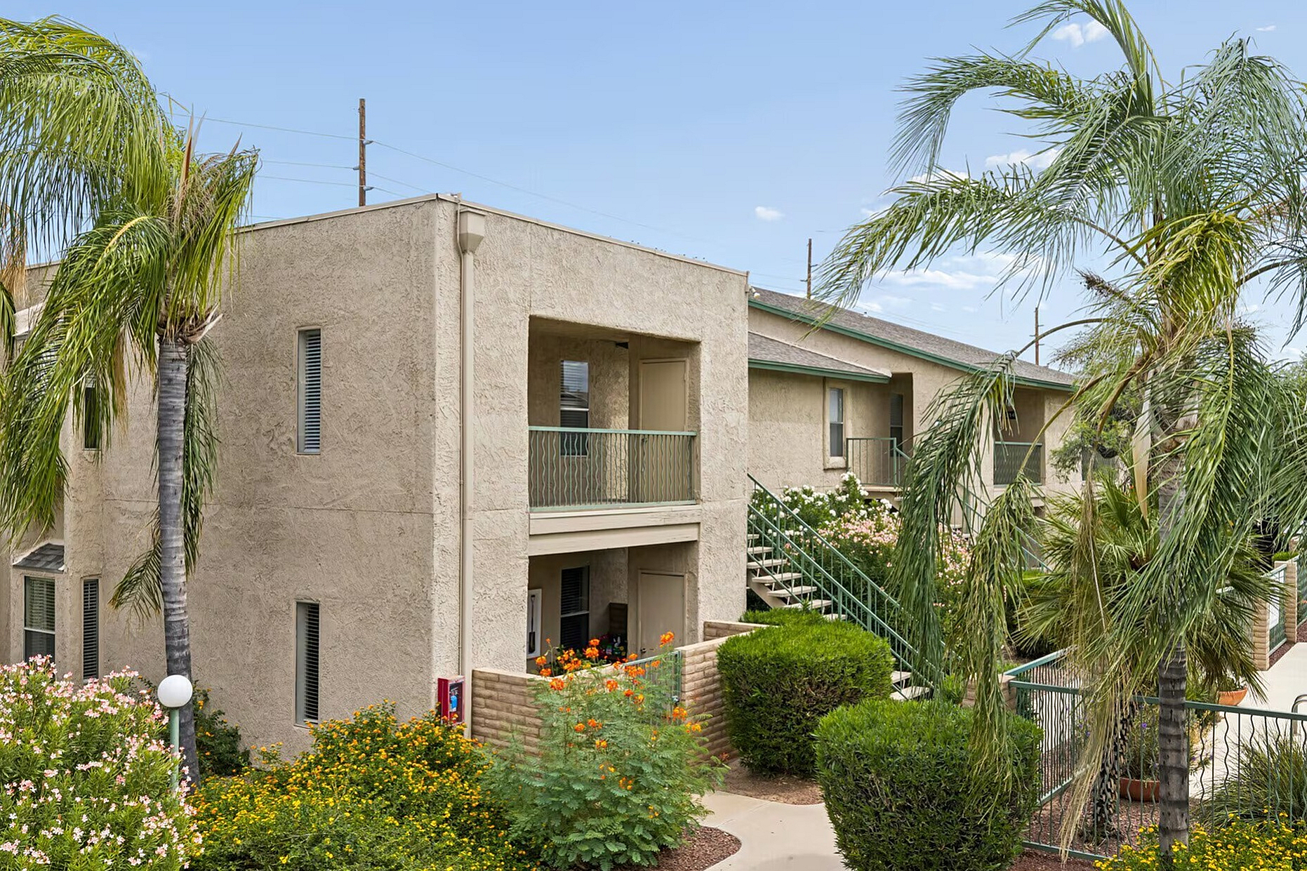 Charming apartment complex with lush landscaping, featuring palm trees, blooming flowers, and inviting exterior design.
