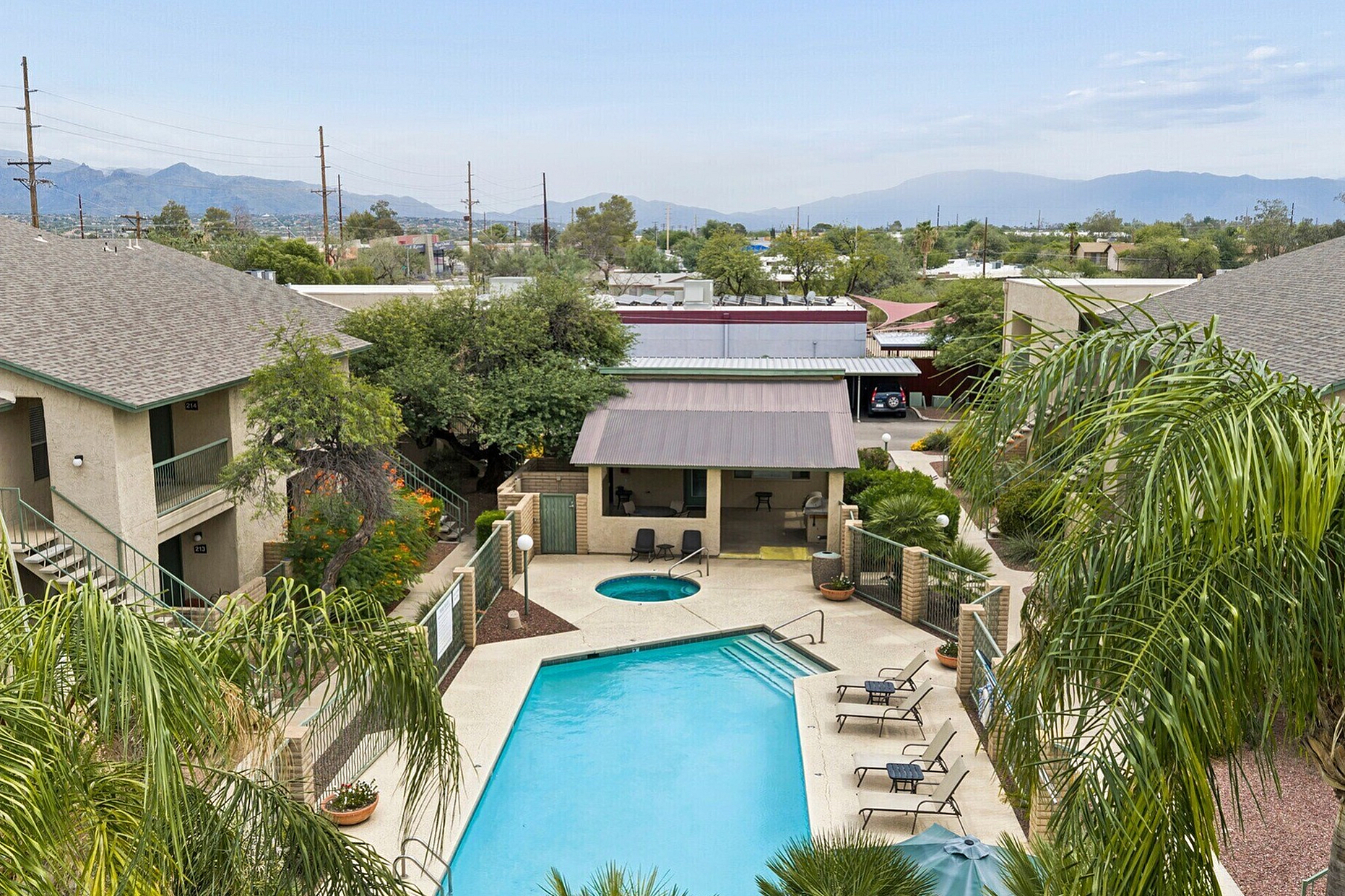 Scenic apartment complex featuring a sparkling pool surrounded by palm trees and a stunning mountain backdrop.