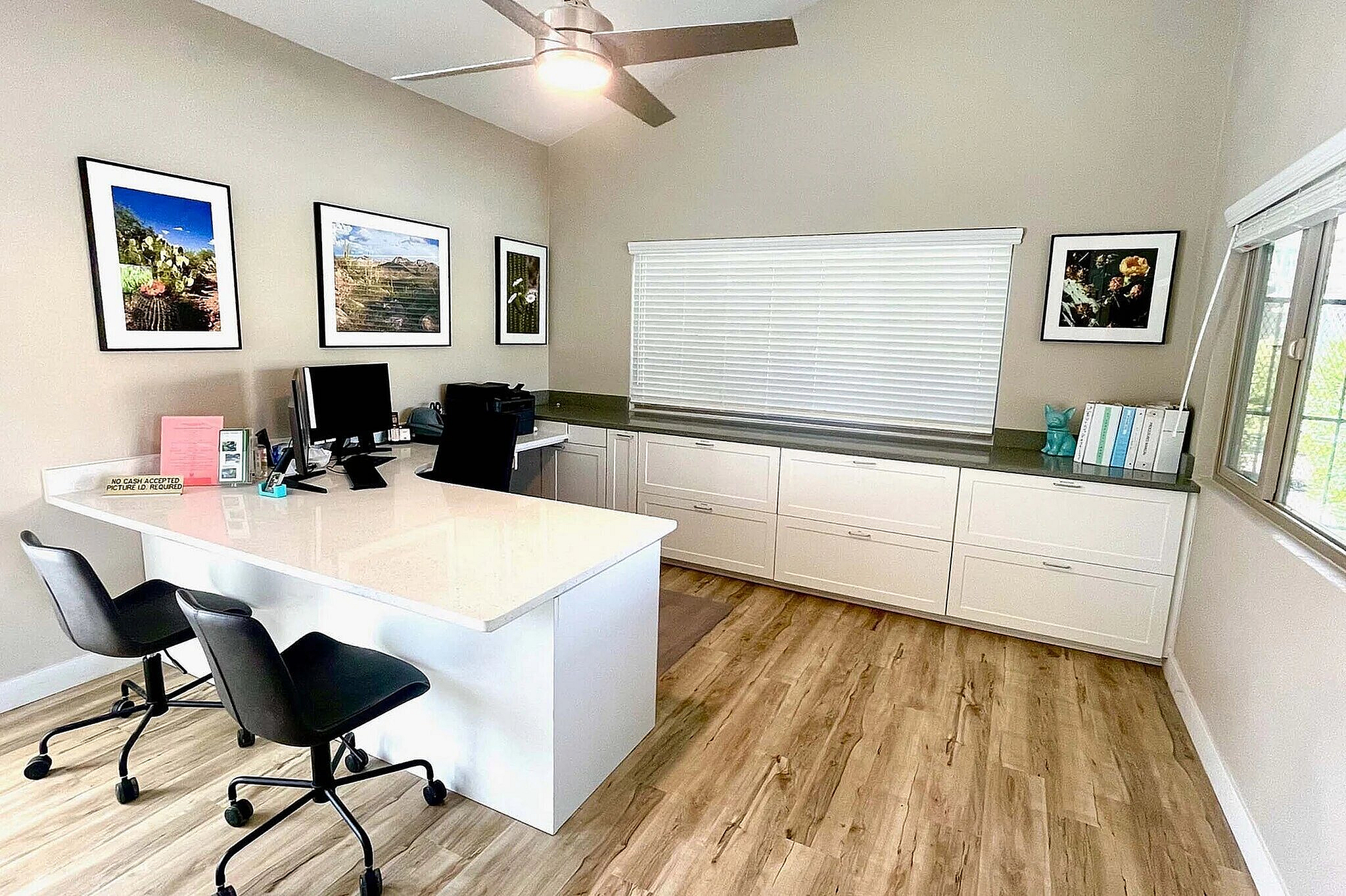 Inviting home office with sleek white desk, modern chairs, and vibrant wall art, featuring ample natural light and elegant laminate flooring.