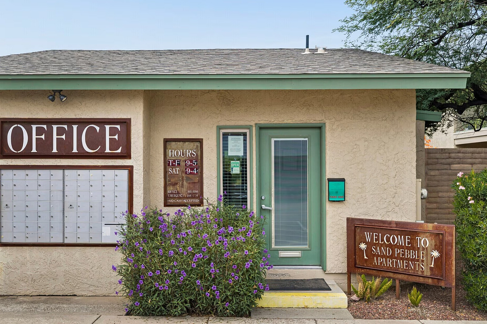 Inviting entrance of Sand Pebble Apartments office with a welcoming sign and lush greenery, highlighting friendly and accessible community services.