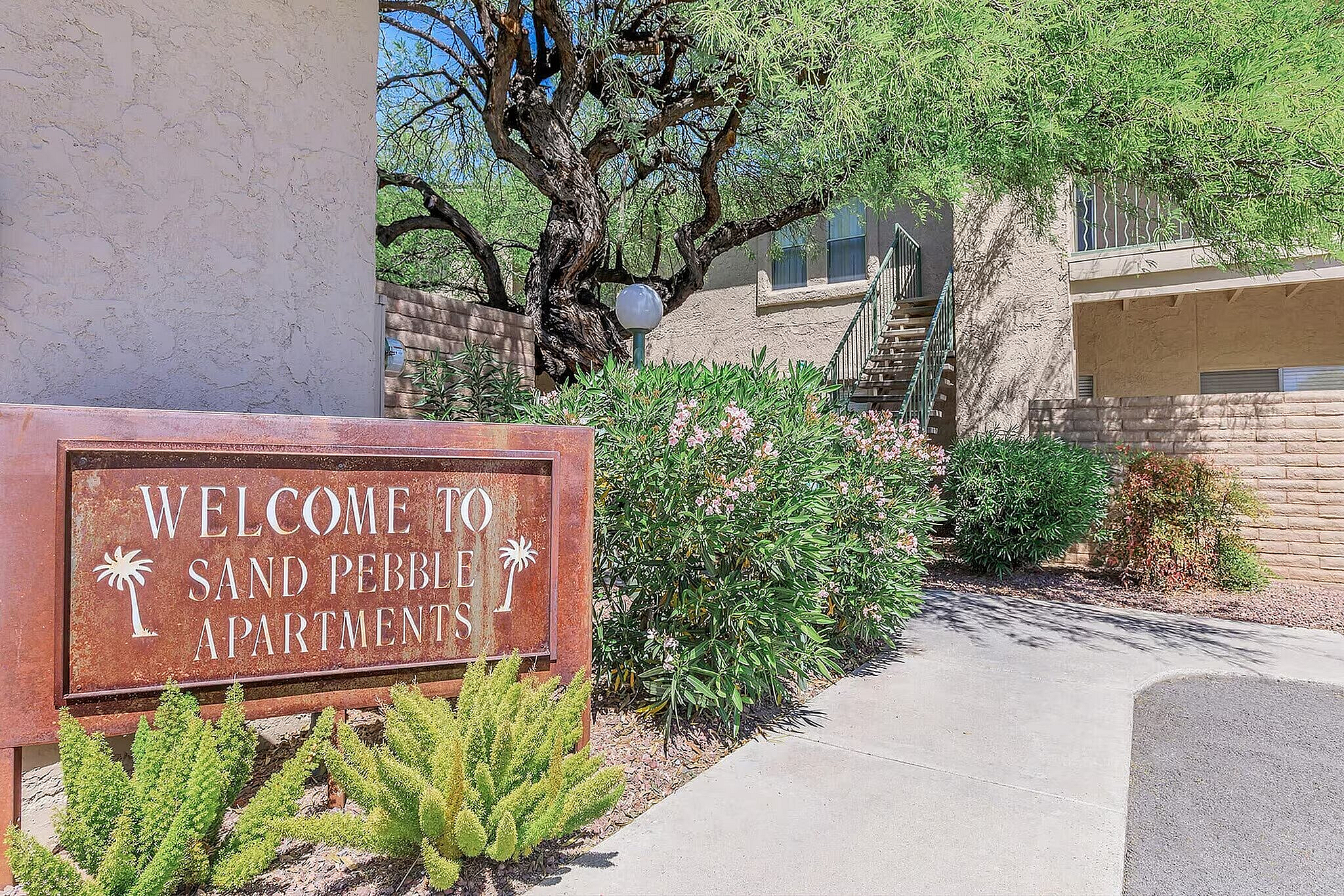 Charming entrance to Sand Pebble Apartments with lush greenery and welcoming signage.
