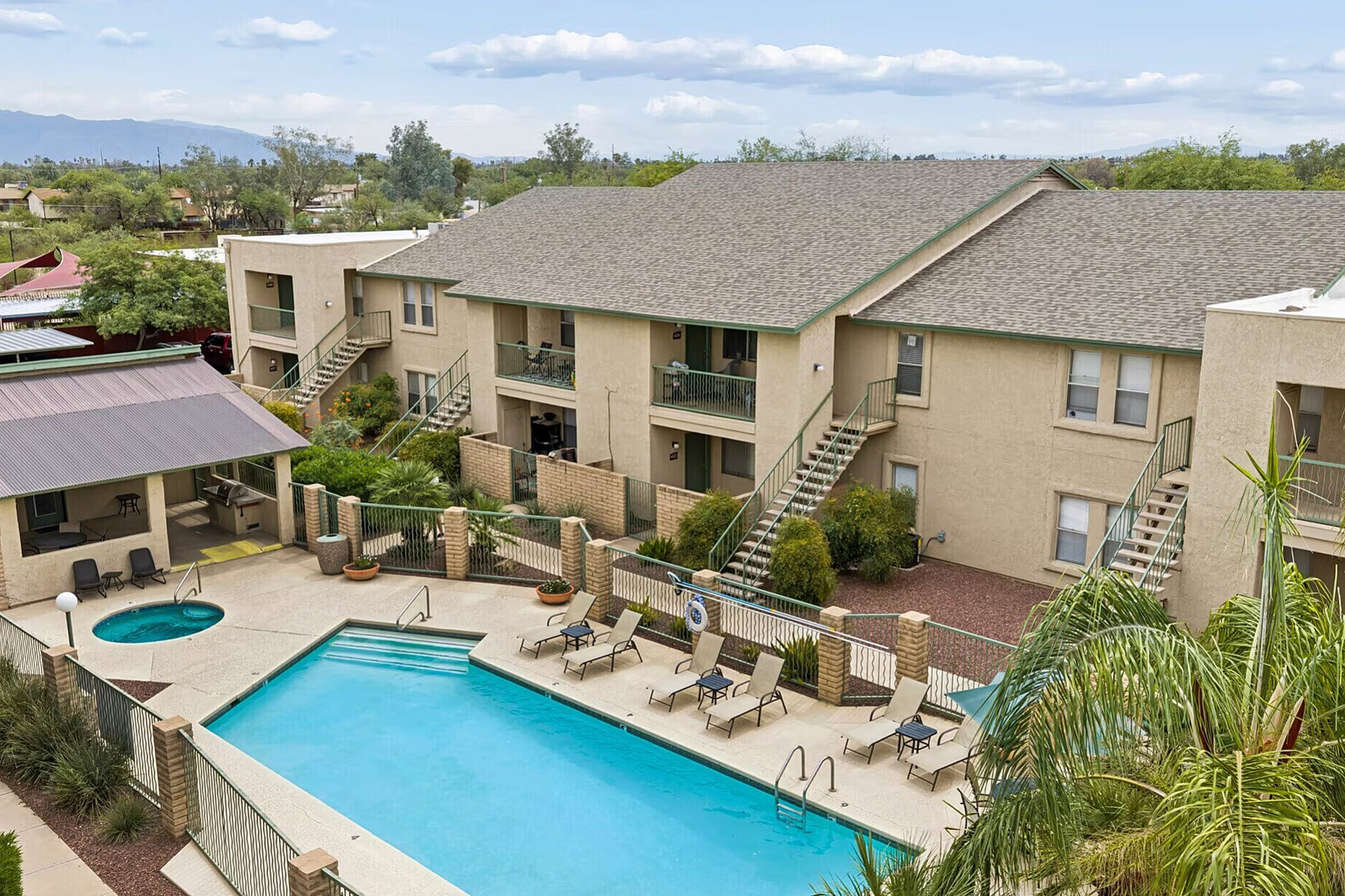 Inviting apartment complex featuring a sparkling swimming pool, relaxing lounge chairs, and lush greenery, offering a serene and comfortable living environment.