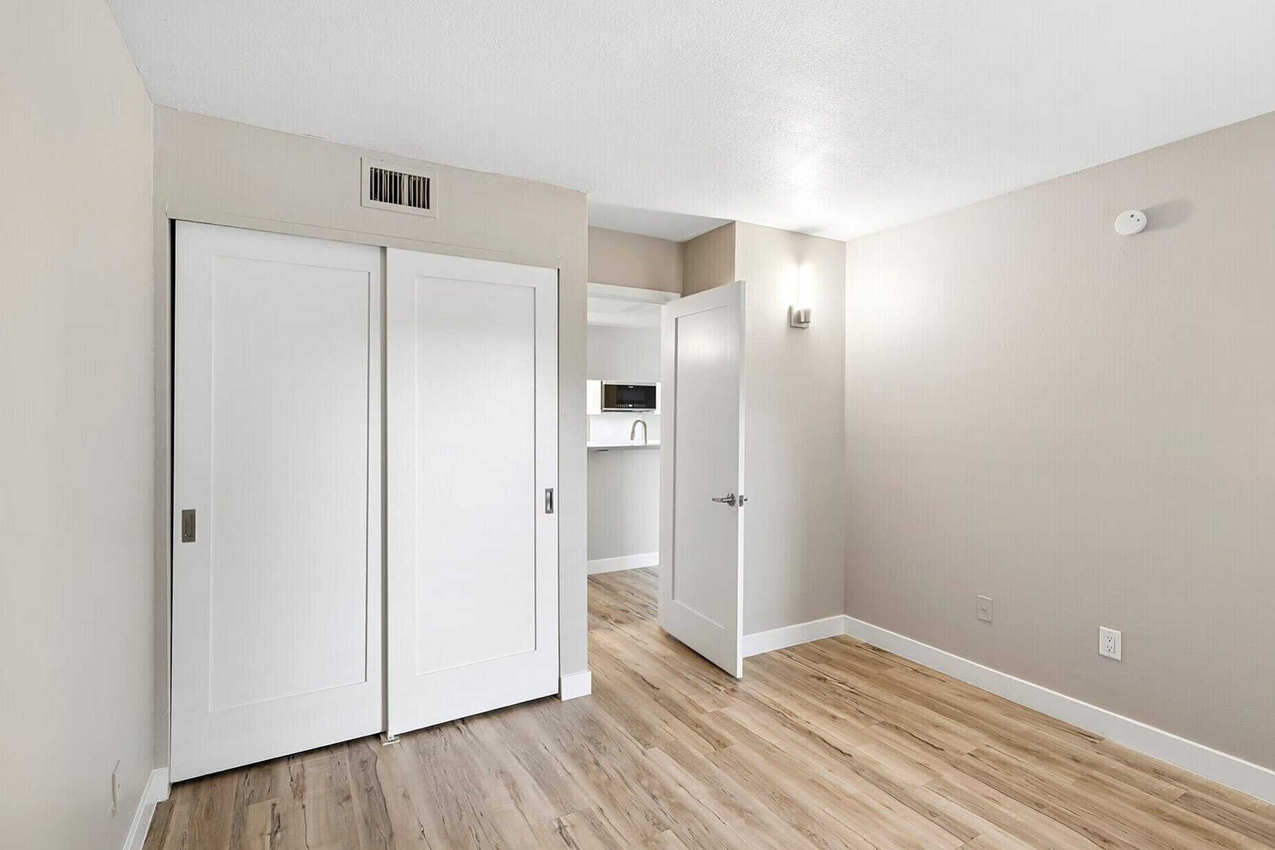 Bright modern interior featuring sleek hardwood floors, a spacious closet with sliding doors, and a stylish open doorway leading to the contemporary kitchen.