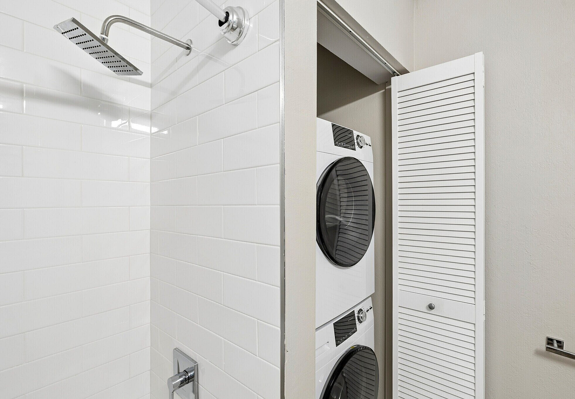 Modern apartment bathroom with sleek white tiles and in-unit stacked washer and dryer.