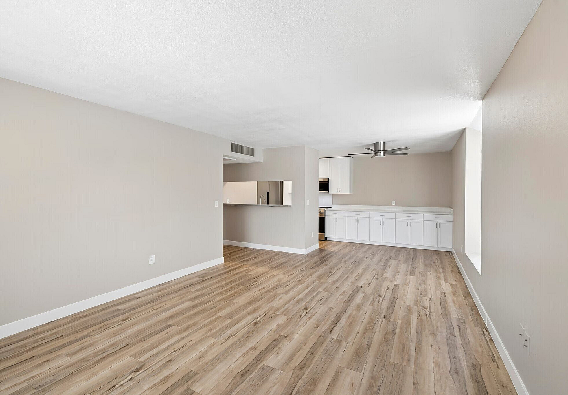 Inviting open-plan living area with elegant wood flooring, modern ceiling fan, and sleek white cabinets for ample storage.