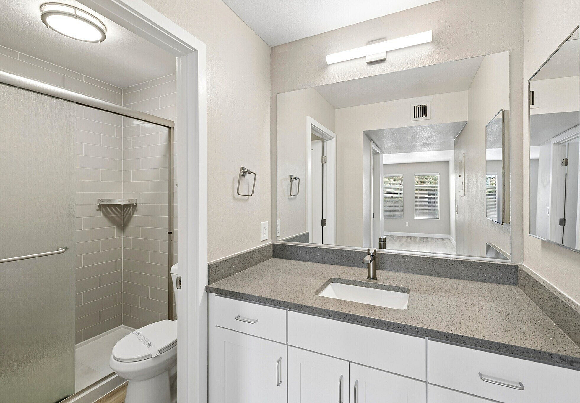 Elegant bathroom featuring a modern vanity with a sleek countertop, stylish lighting, and a spacious walk-in shower. Bright windows enhance the contemporary design.