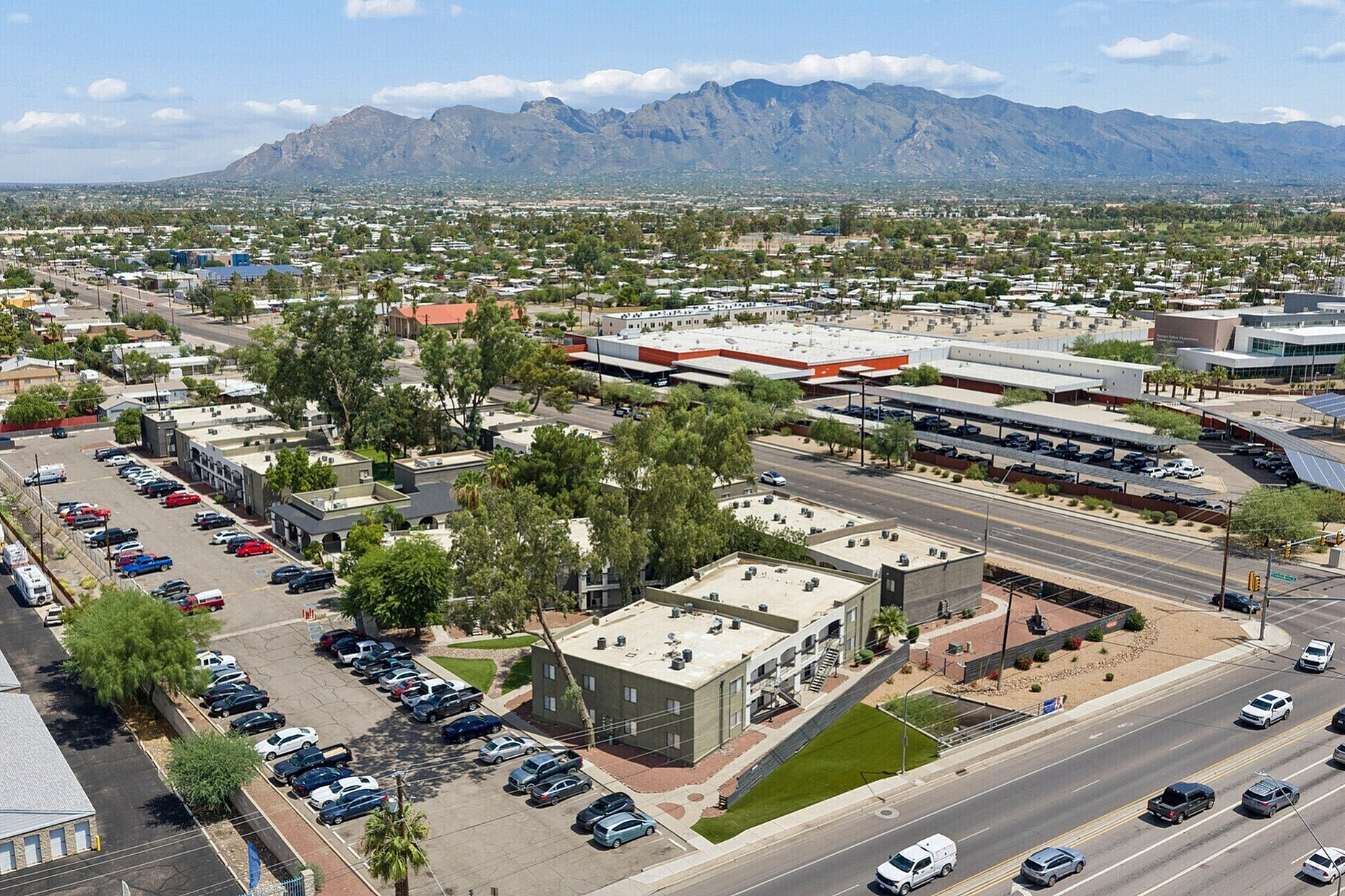 Aerial view showcasing a vibrant urban neighborhood with charming apartment complexes surrounded by lush greenery, expansive parking, and scenic mountain vistas.