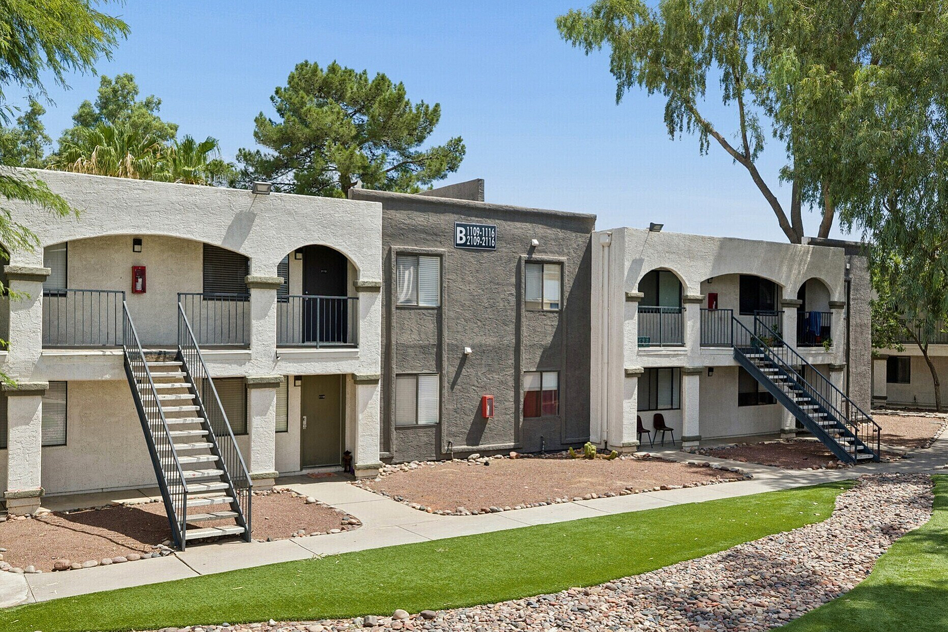 Charming apartment complex with modern design featuring stone pathways, lush greenery, and inviting balconies.