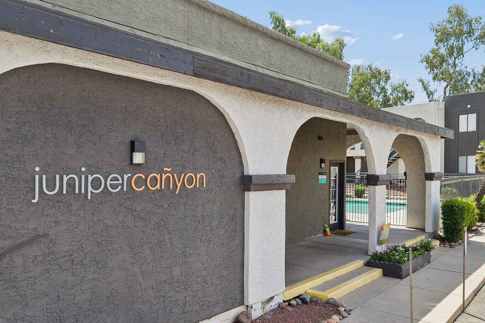 Charming entrance of Juniper Canyon with elegant arches, lush greenery, and inviting modern design.