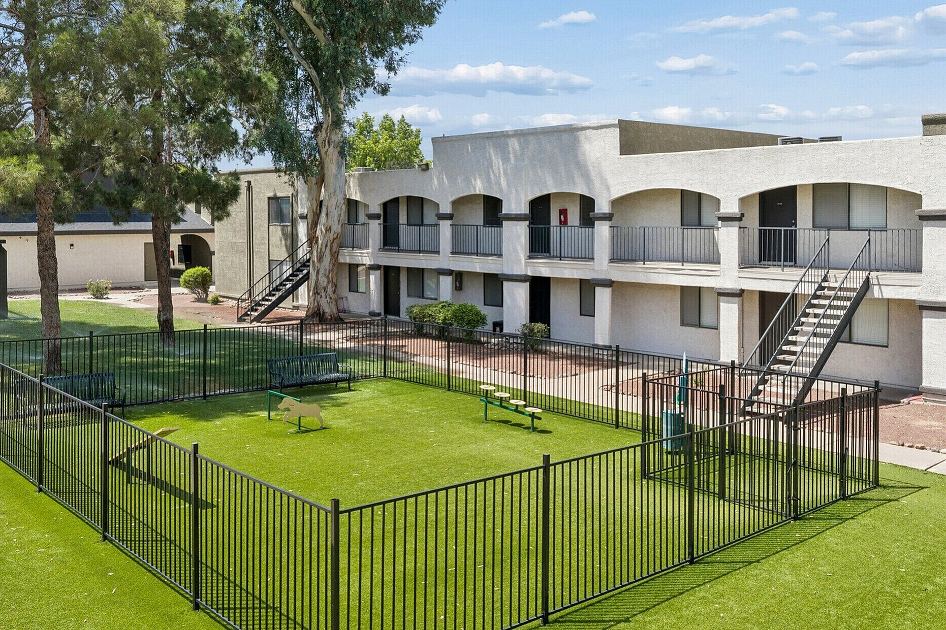 Charming apartment building with a lush green pet-friendly area, surrounded by mature trees and modern architecture.