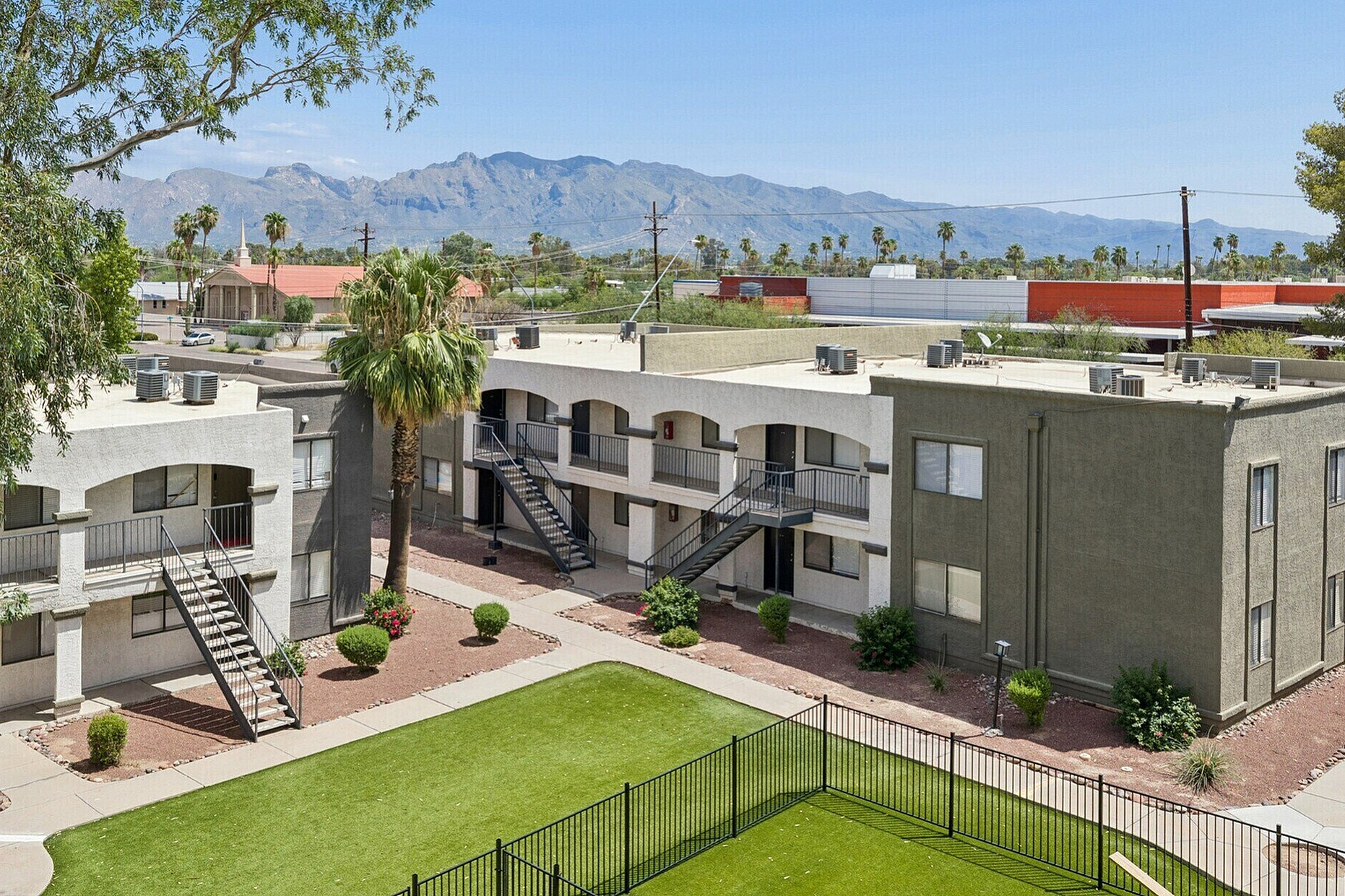 Charming apartment complex with lush green courtyard, majestic mountain views, and elegant staircases leading to spacious units.
