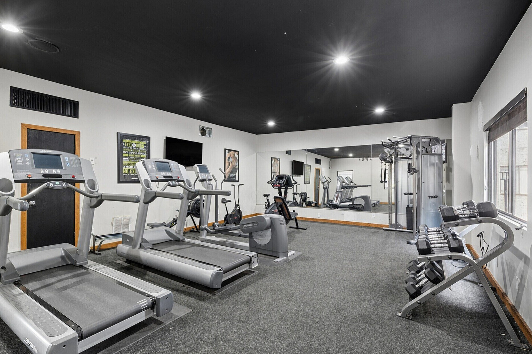 Modern fitness center with state-of-the-art treadmills, weight rack, and exercise machines, offering a bright and spacious workout environment.