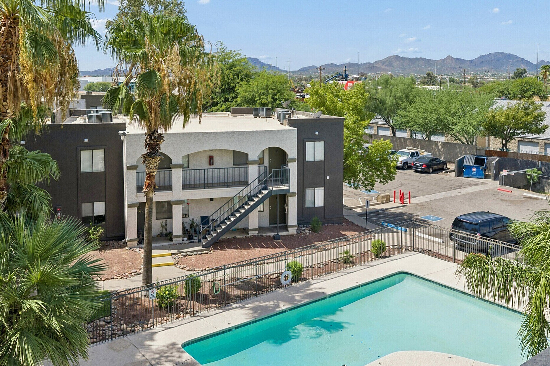 Charming apartment complex surrounded by lush palm trees featuring a modern exterior and inviting swimming pool; perfect for relaxation and enjoying scenic mountain views.