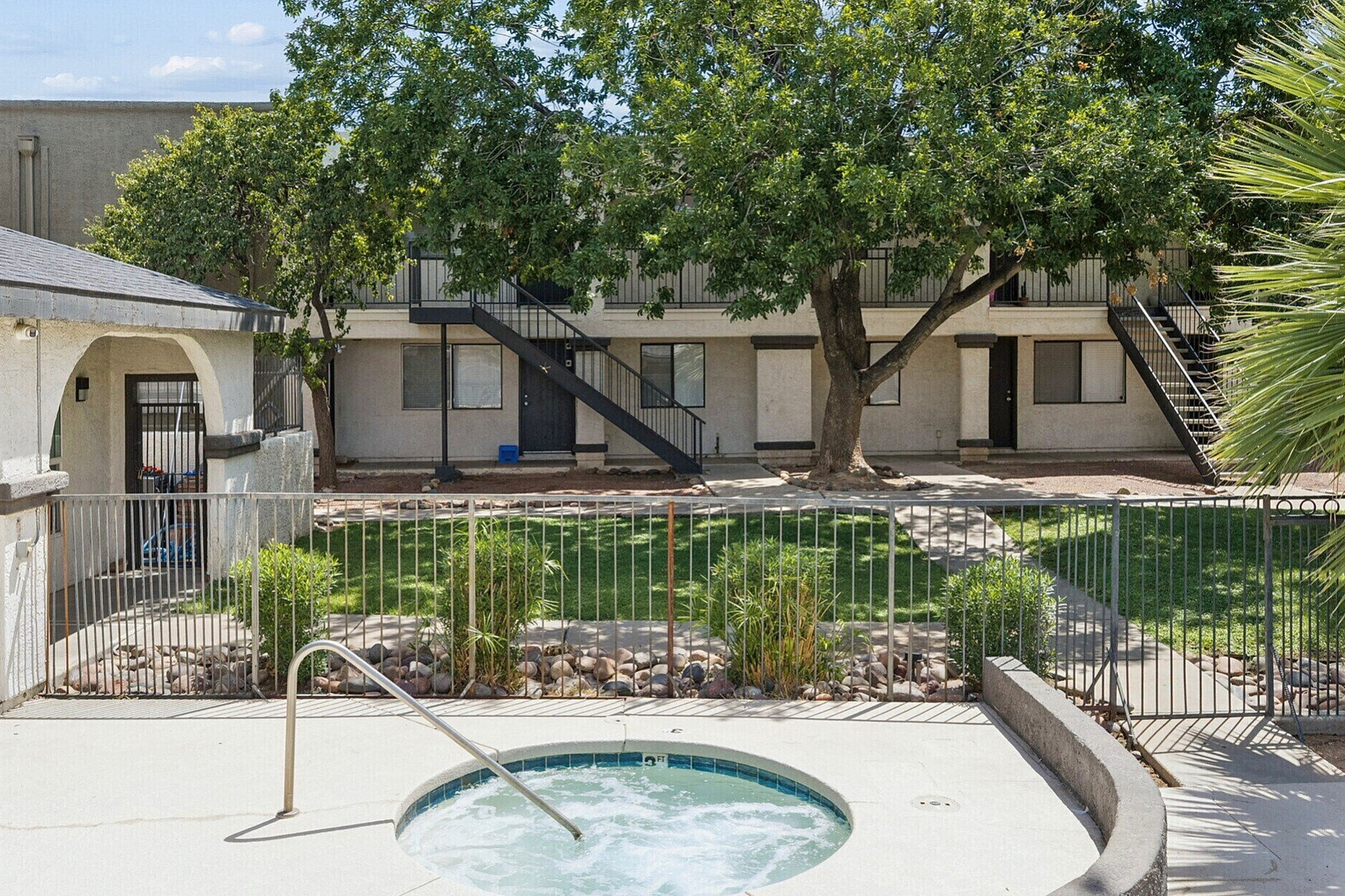 Charming apartment complex featuring a tranquil courtyard, lush greenery, and inviting hot tub area.