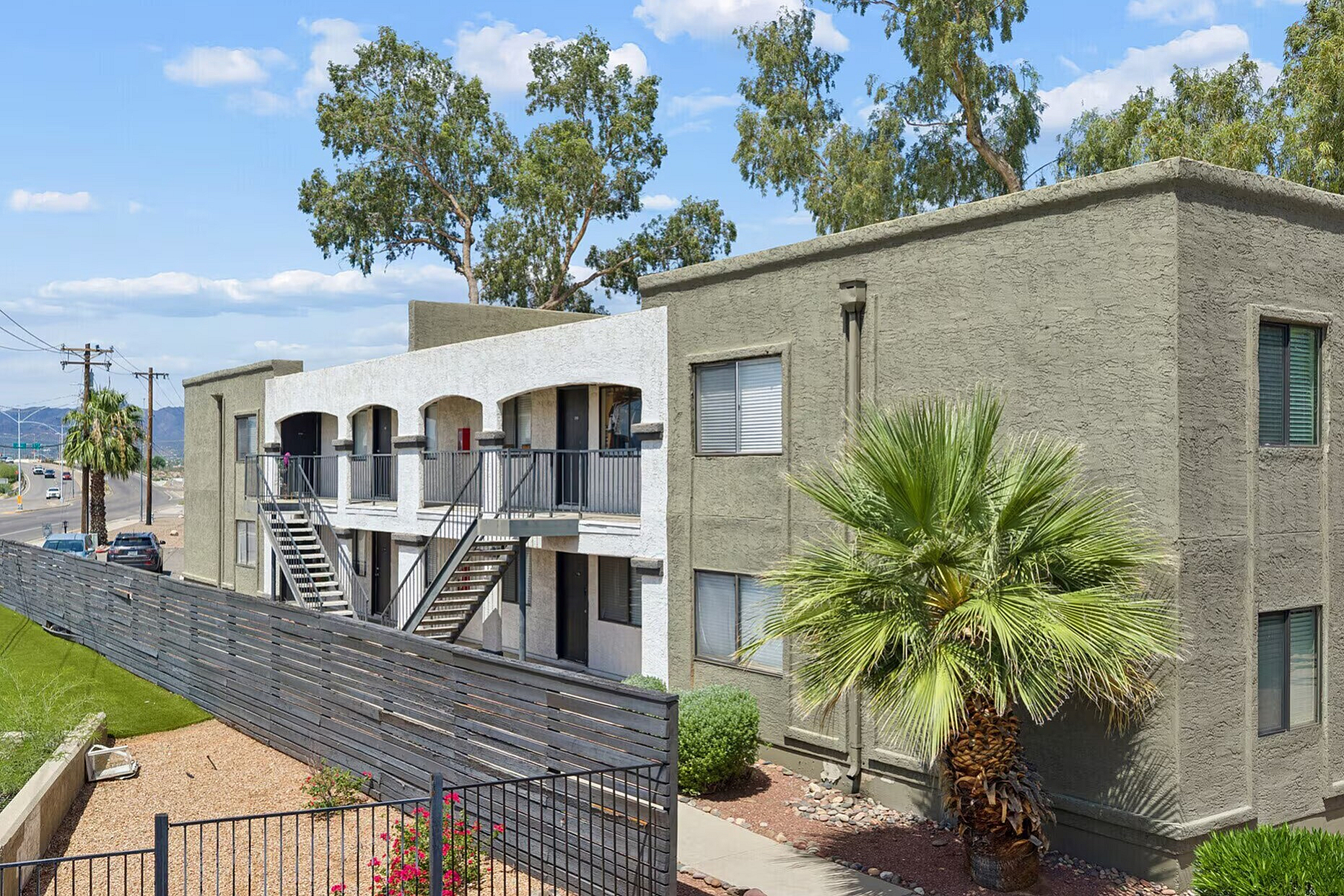 Modern apartment complex with charming stucco exterior, lush palm trees, and vibrant landscaping offering scenic mountain views.