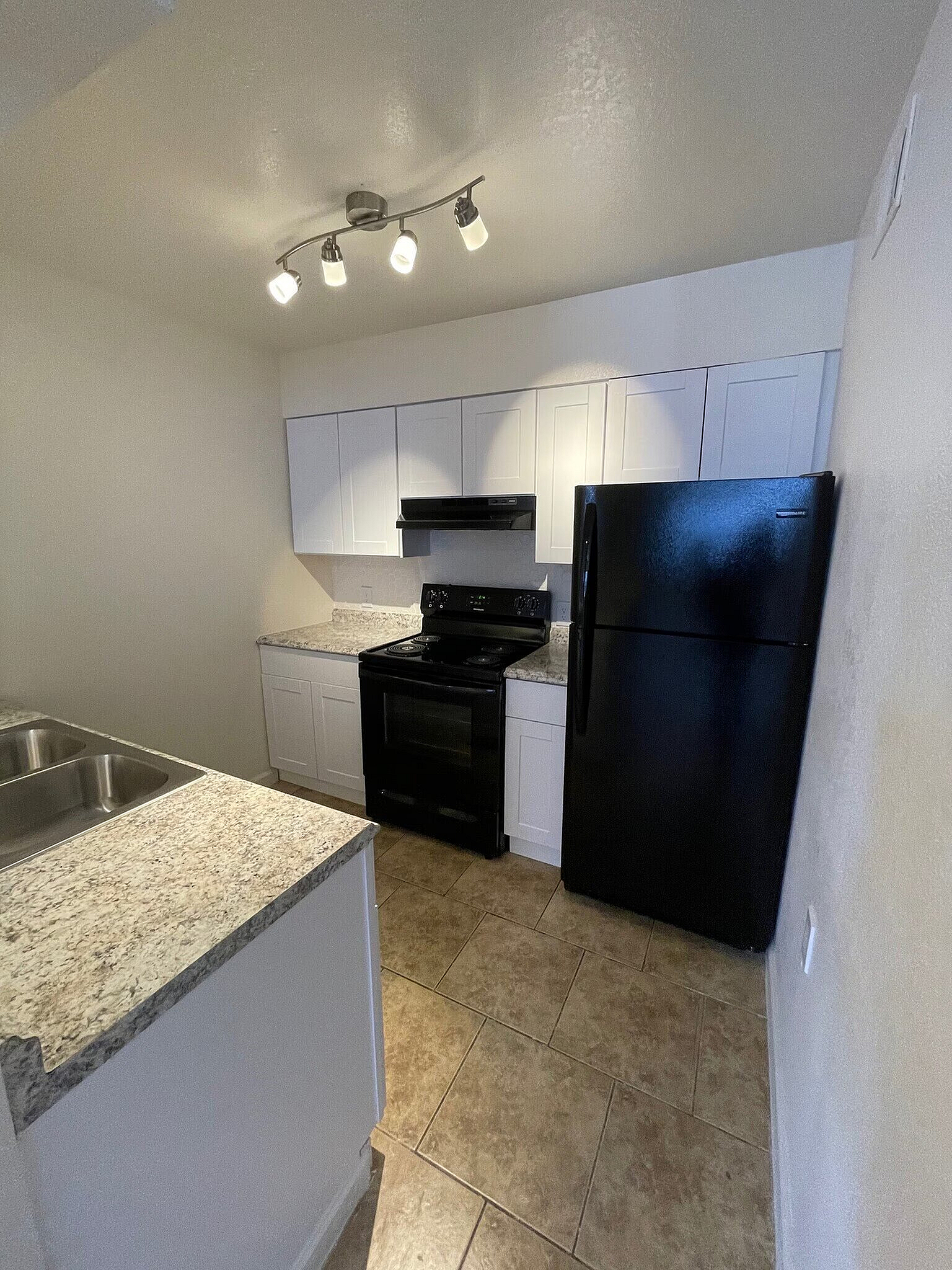 Modern kitchen with sleek granite countertops, stainless steel sink, elegant track lighting, and black appliances for a stylish cooking space.