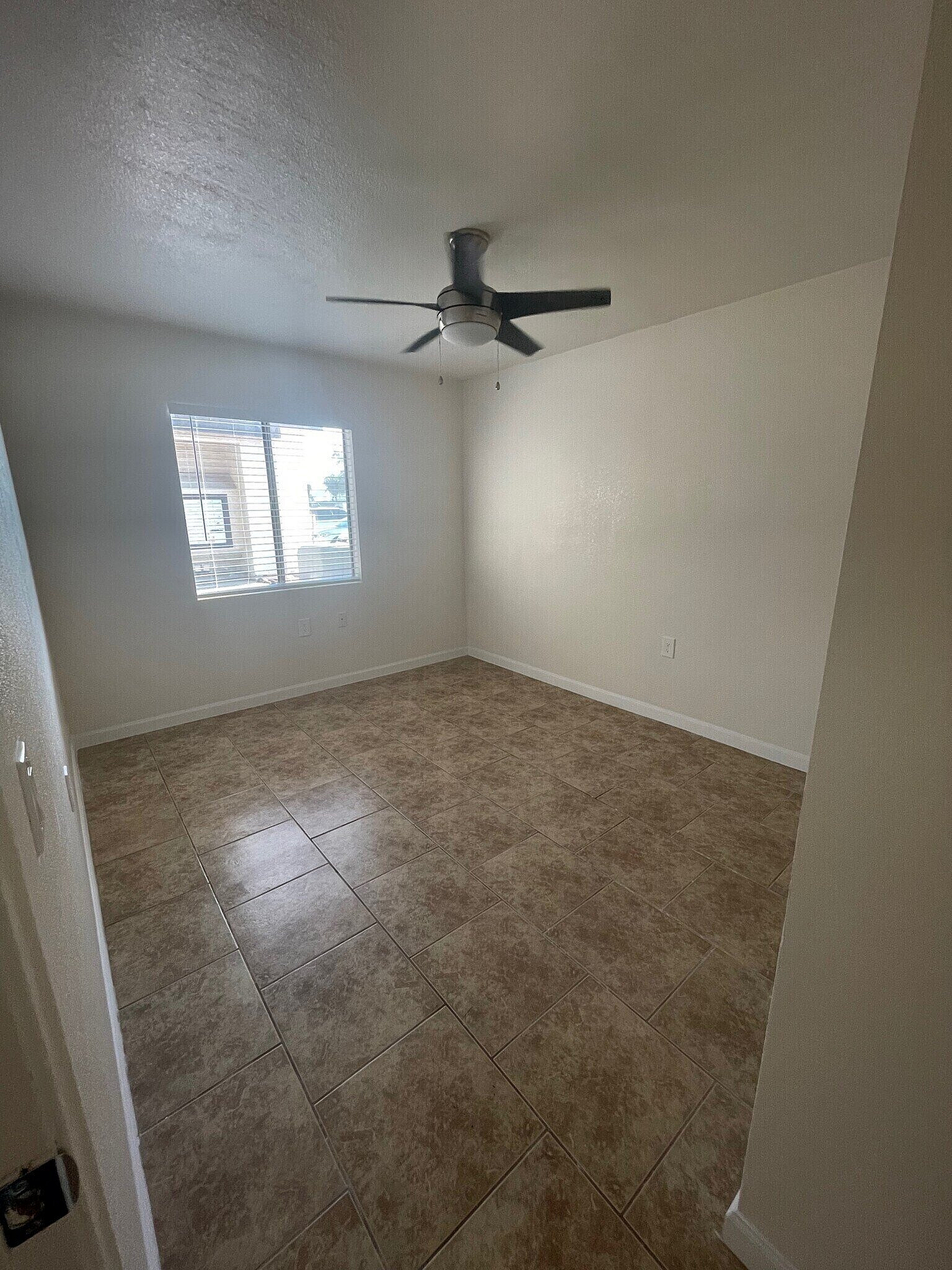 Bright and airy bedroom with large window, elegant ceiling fan, and stylish tiled flooring, offering a tranquil living space.