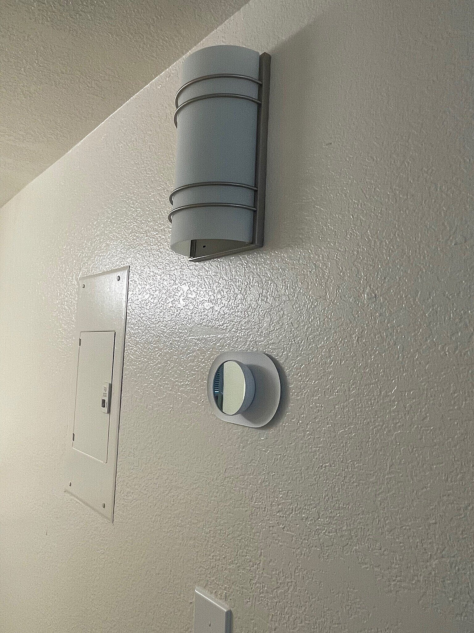 Modern wall featuring sleek light fixture and smart thermostat, highlighting advanced home technology.