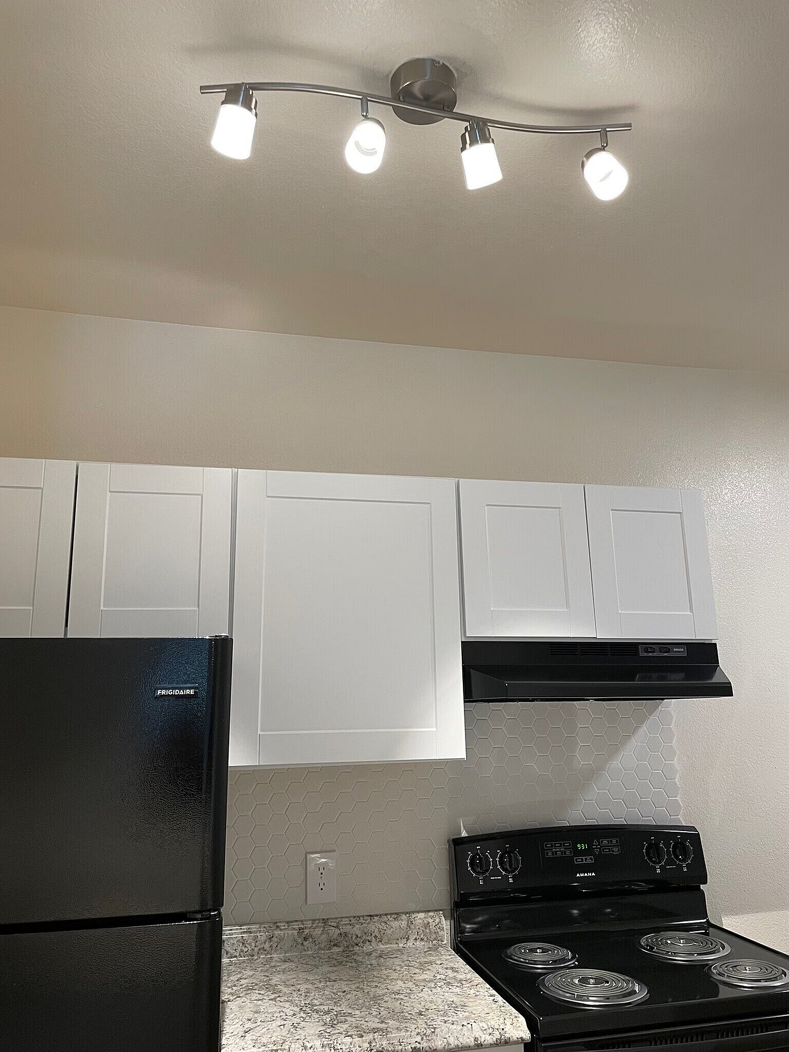 Modern kitchen featuring sleek black appliances, elegant white cabinetry, and stylish track lighting enhancing a chic, contemporary atmosphere.