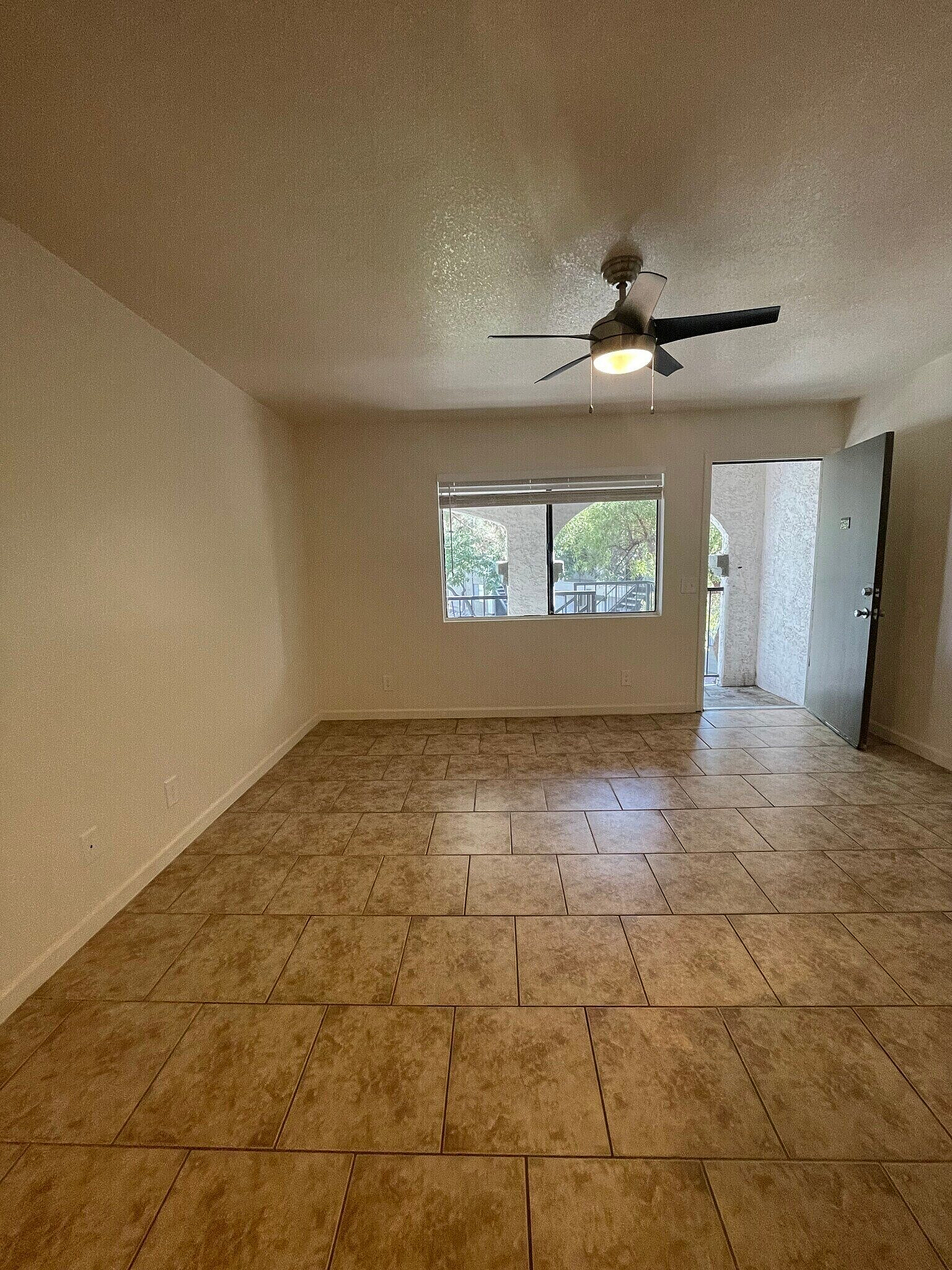 Bright and spacious living area with elegant tile flooring, ceiling fan, and large window offering natural light and charming outdoor views.