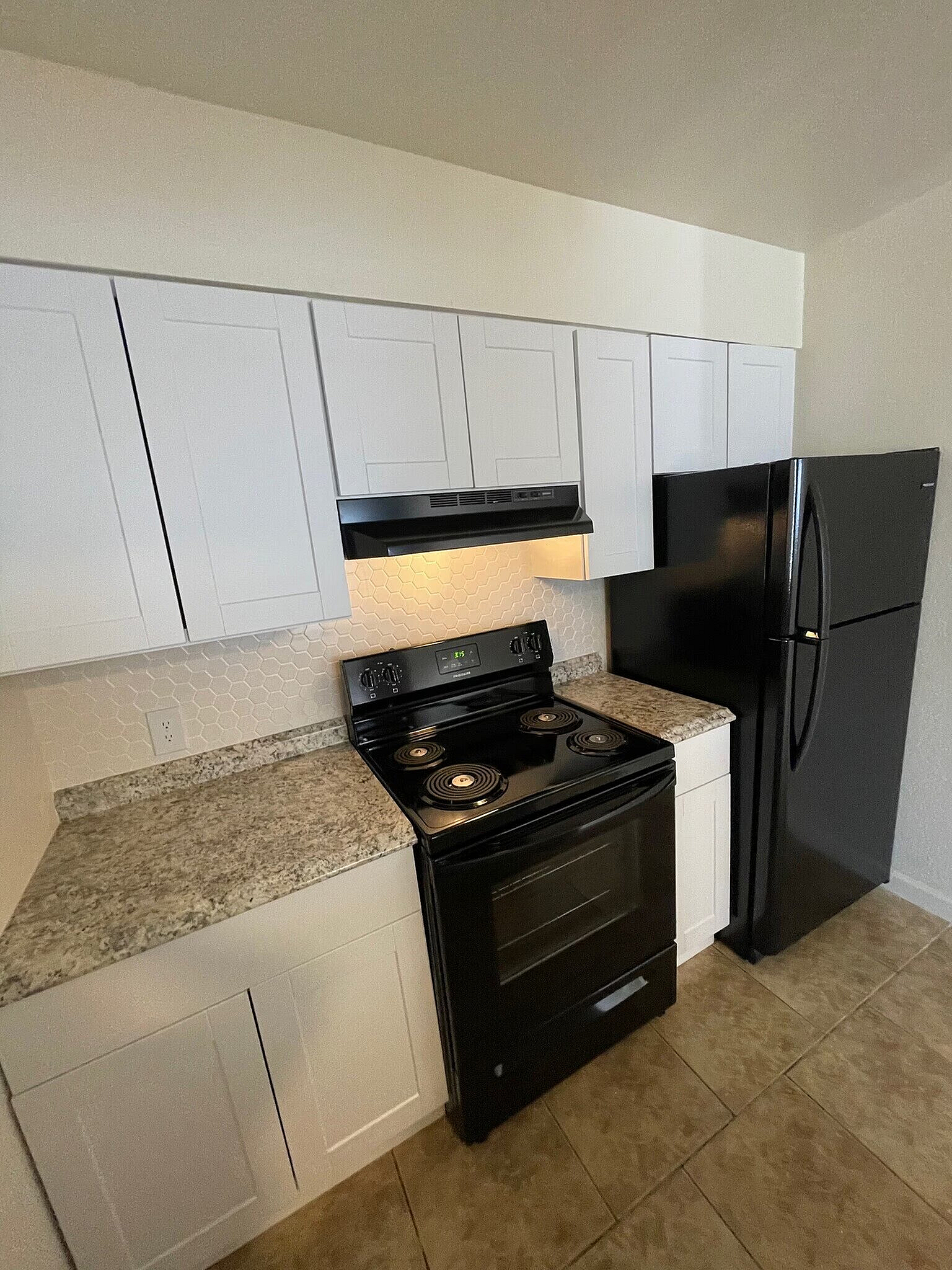 Modern kitchen with sleek white cabinetry, black appliances, and elegant granite countertops.