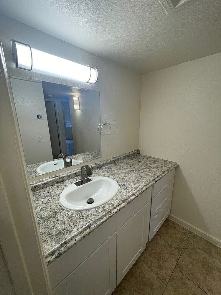 Modern bathroom with elegant granite countertop and sleek white cabinetry, illuminated by contemporary lighting.