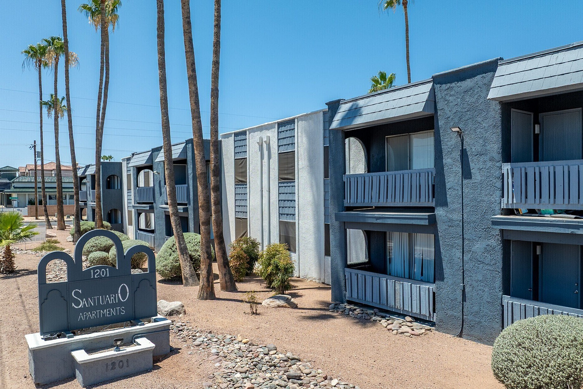 Charming desert-style apartment complex with modern balconies, surrounded by tall palm trees and a serene landscape.