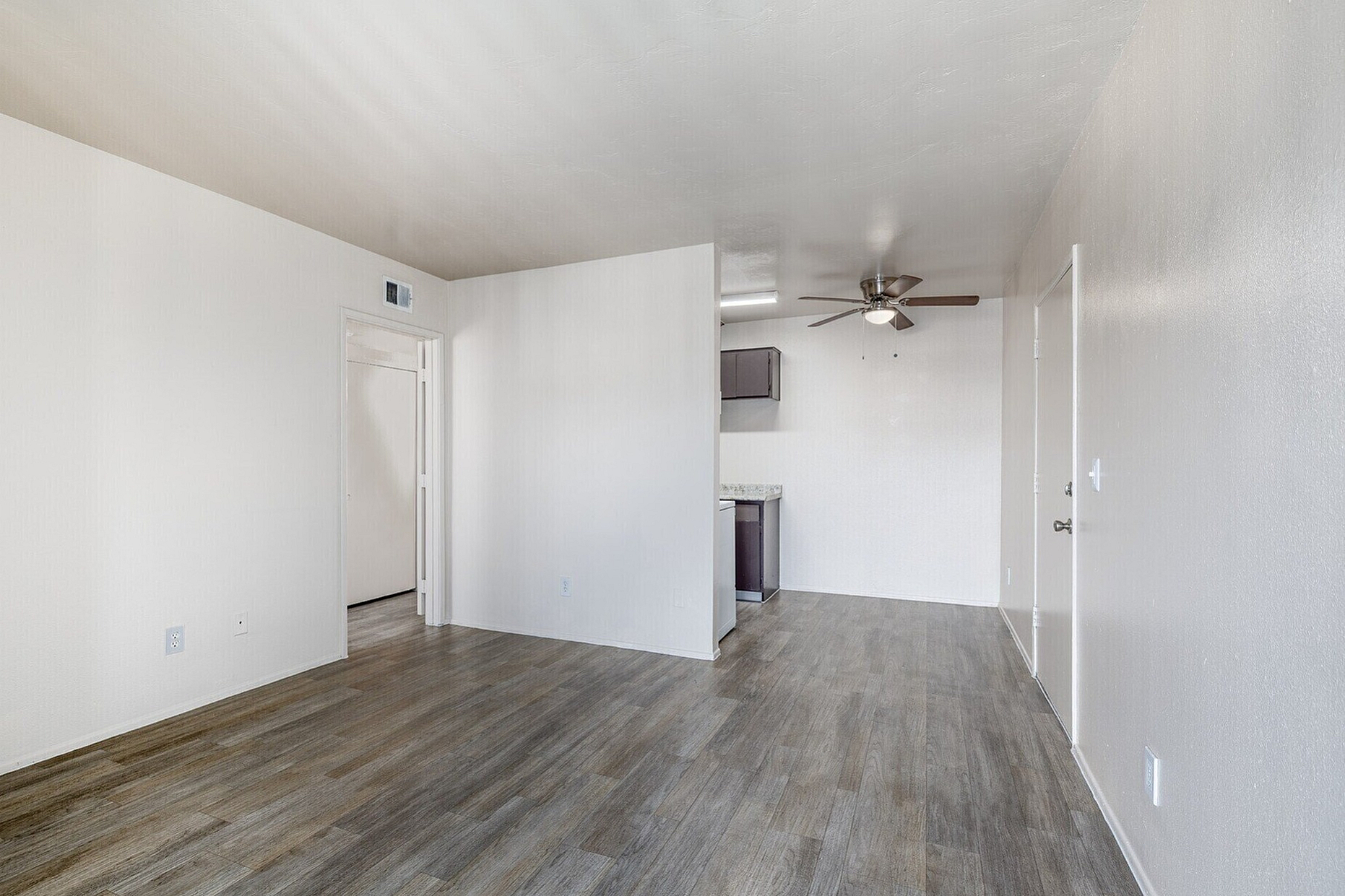 Chic open-concept apartment with elegant wood flooring and modern ceiling fan, leading to a cozy kitchen.