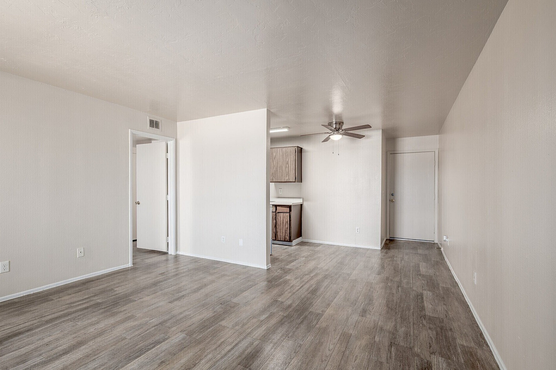 Open and inviting apartment living area with modern wooden flooring, ceiling fan, and natural light enhancing the space.