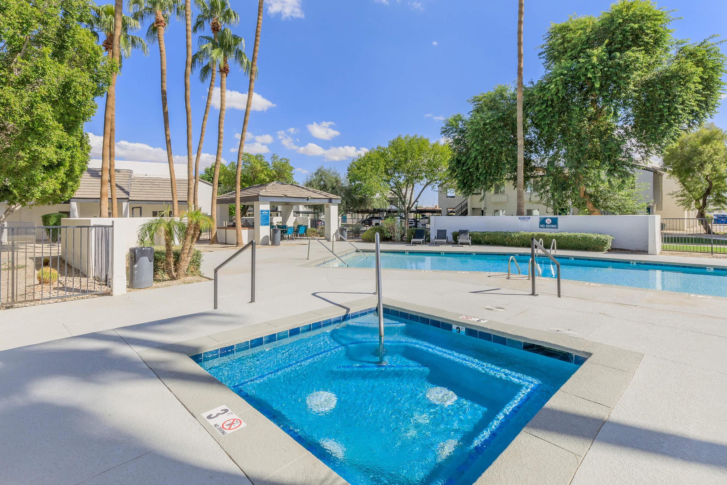 Lush oasis featuring a sparkling pool and spa surrounded by palm trees and modern amenities, ideal for relaxation in a sunny setting.