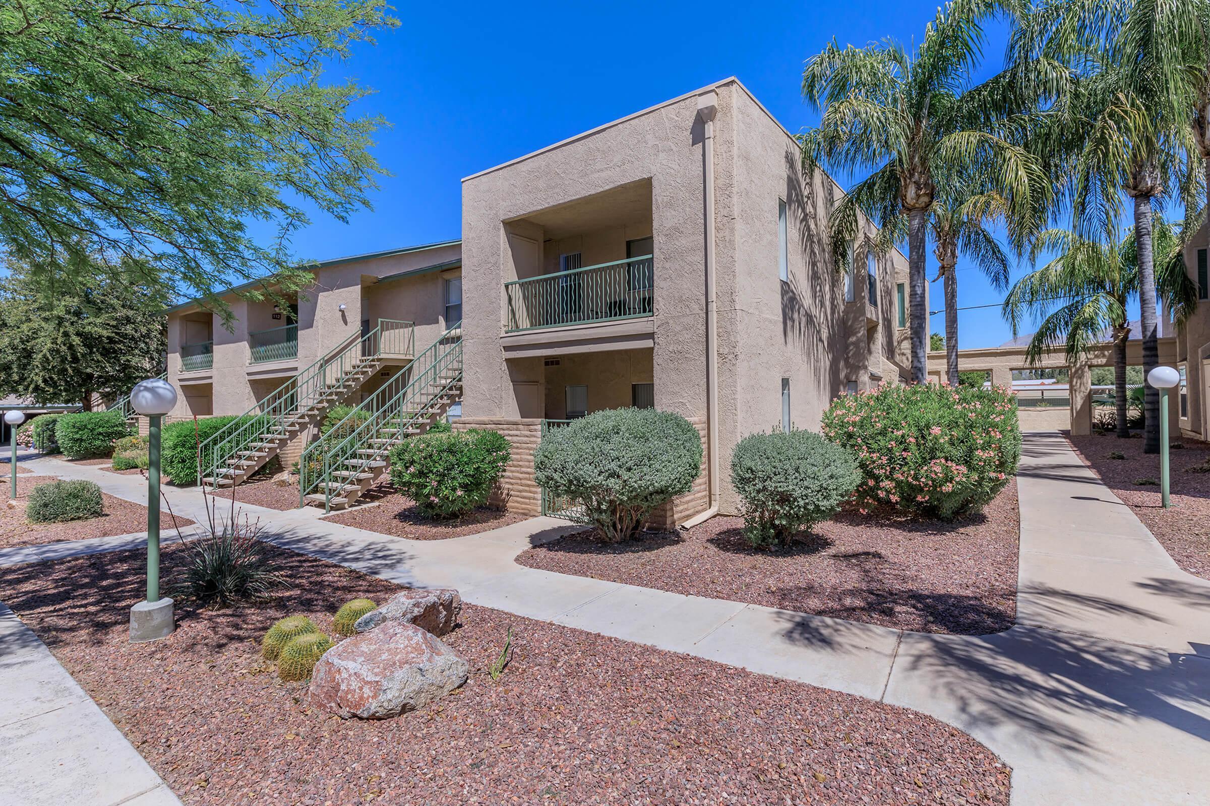Charming apartment exterior surrounded by lush greenery and vibrant desert landscaping, featuring modern architectural design and inviting walkway.