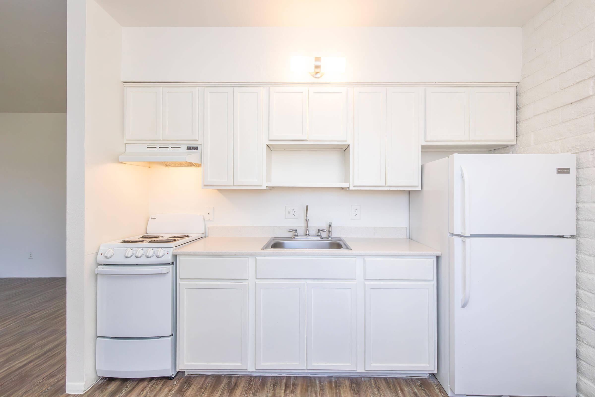 Bright, modern kitchen with sleek white cabinetry, compact stove, and spacious refrigerator, set against a stylish brick accent wall.